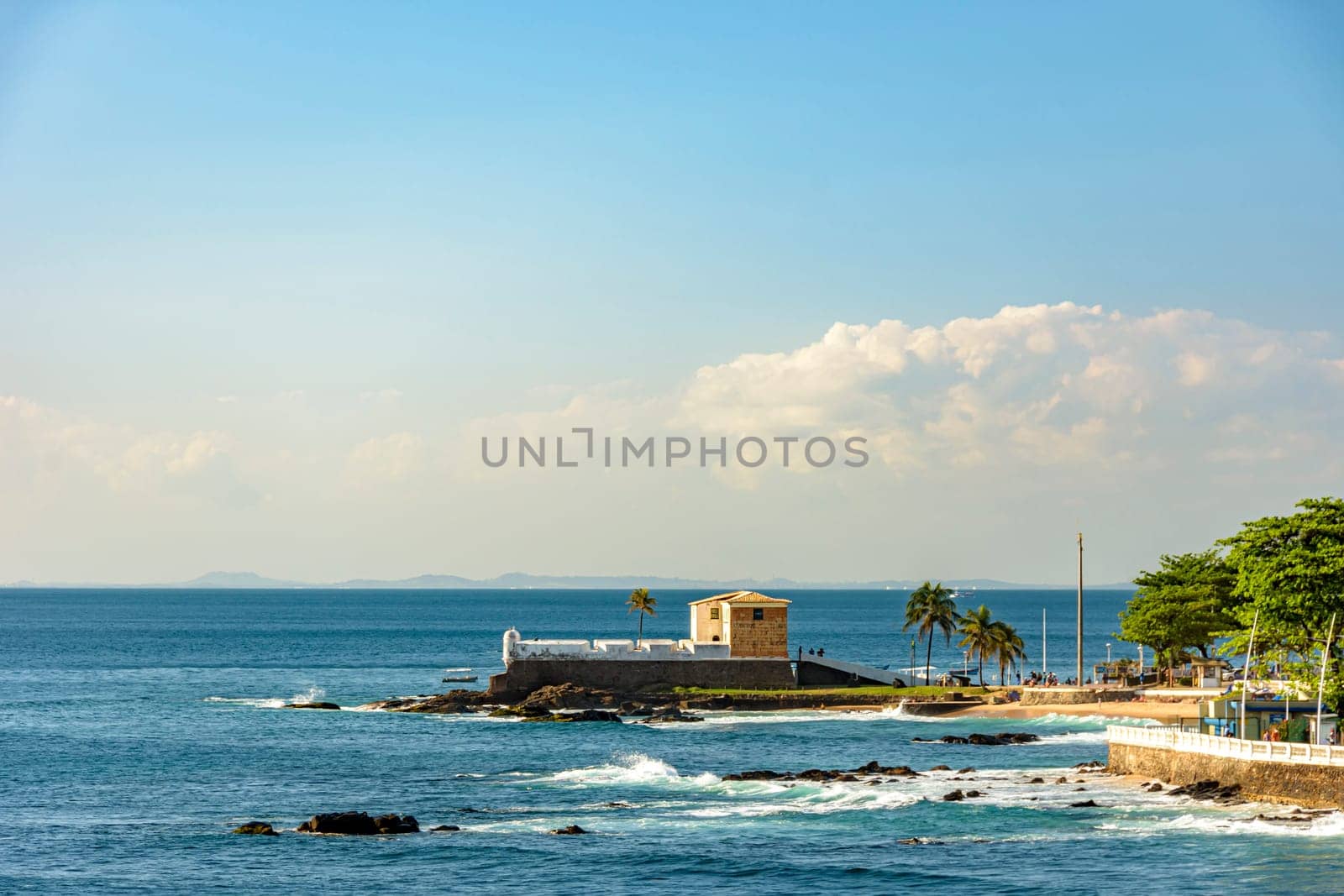 Scenic view of the old colonial Portuguese Fort Santa Maria in Barra beach, Salvador, Brazil with palm trees standing above the rugged shoreline