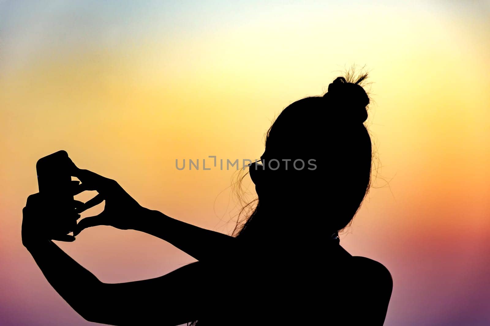 Silhouette of girl with smartphone taking selfie in the summer during the sunset