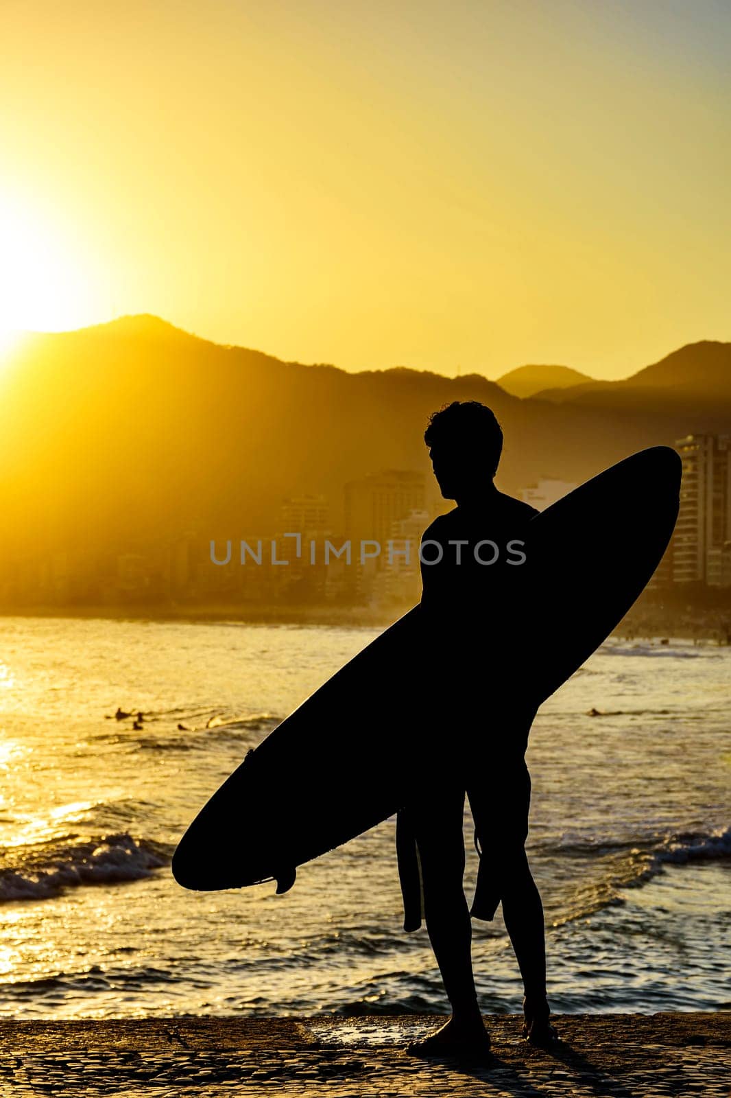 Surfer silhouette with his longboard looking at the Iapnema beach waves in Rio de Janeiro during sunset