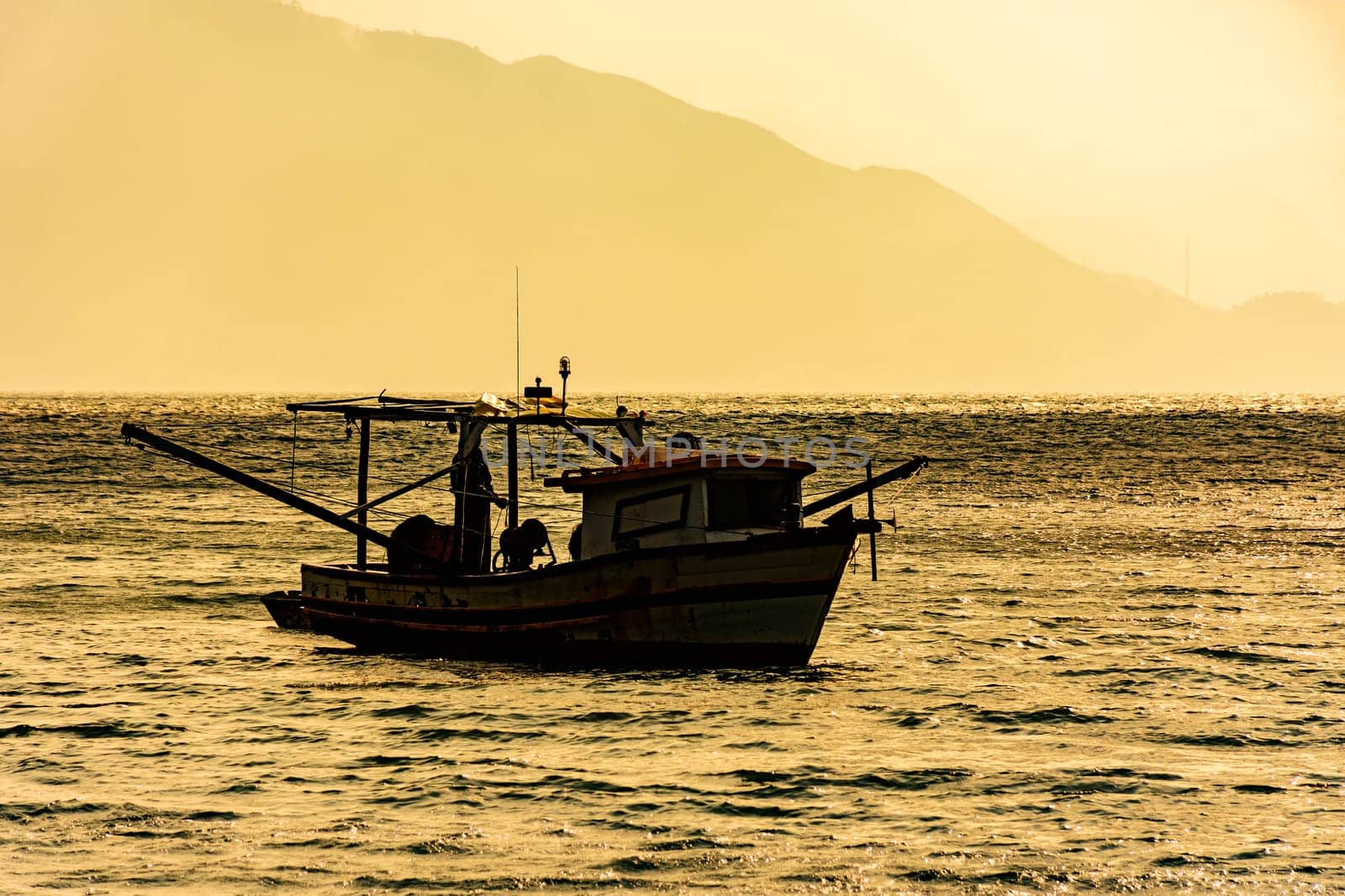 Wooden trawler used for fishing floating on the sea at sunset in Ilhabela on the coast of Sao Paulo, Brazil