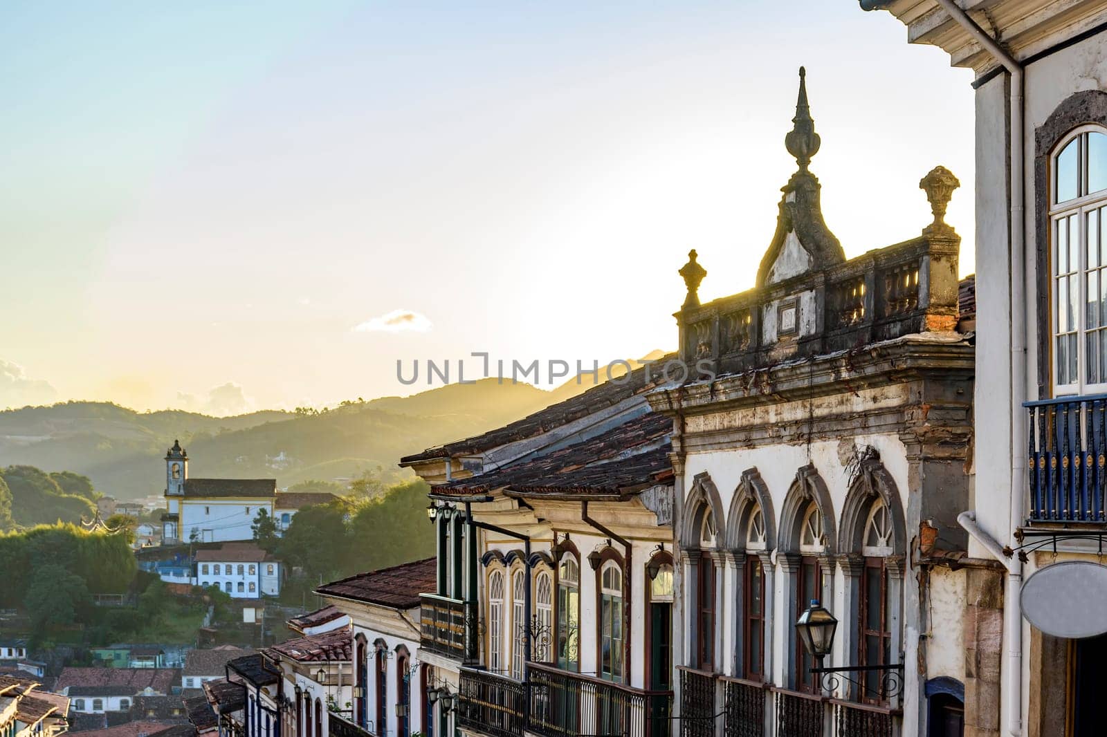 View of colonial style houses facade and historic baroque church in the background on the hills of Ouro Preto city, Minas Gerais state, Brazil