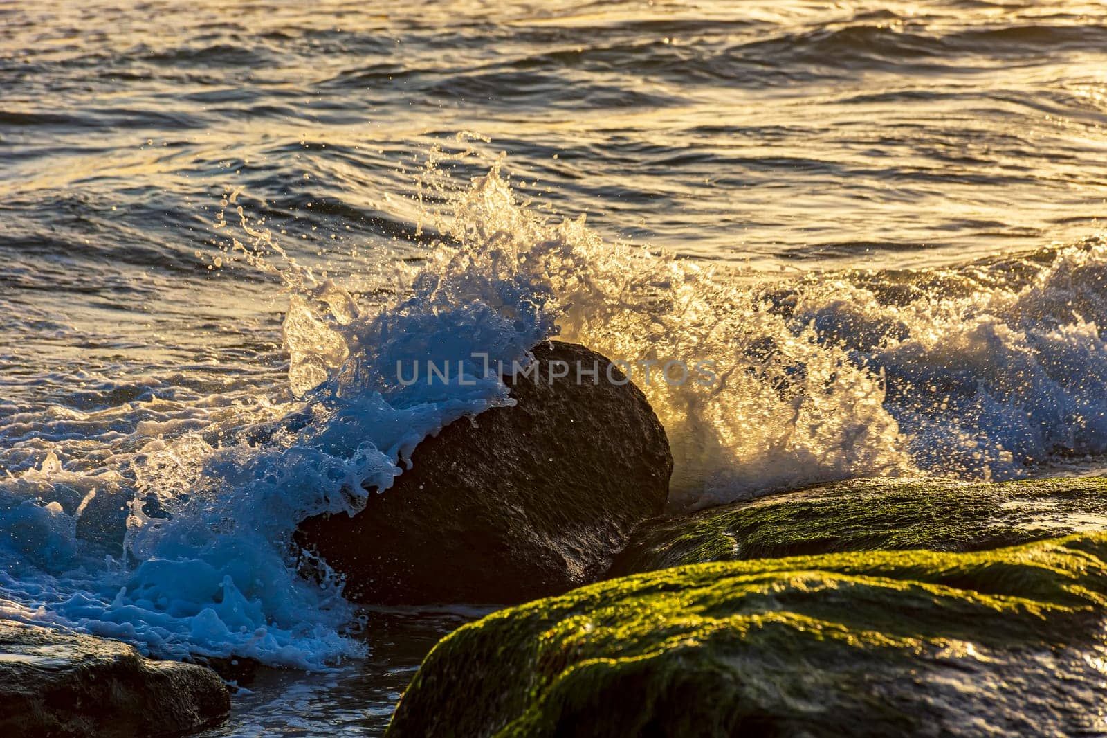 Water and sea foam splashing with waves crash against rocks during tropical sunset