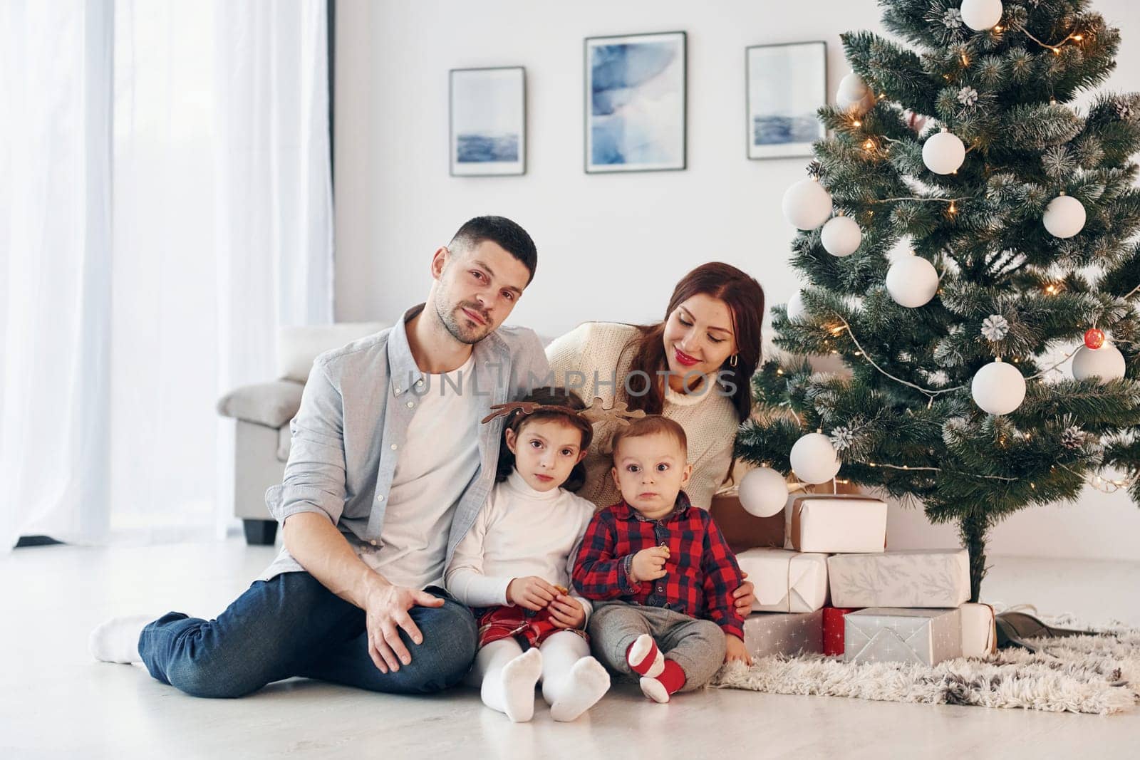 Sits against fir. Beautiful family celebrates New year and christmas indoors at home.