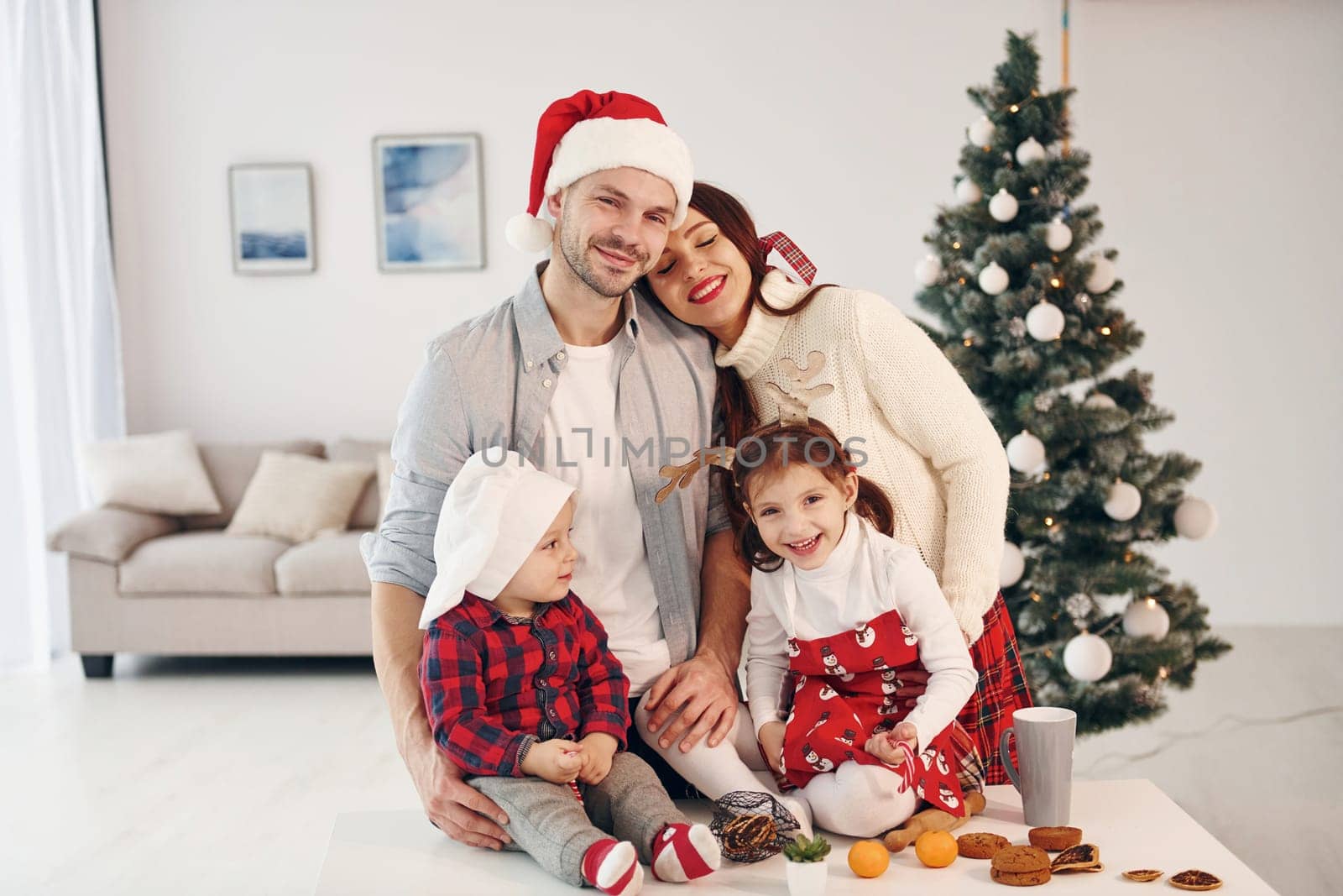 Sits against fir. Beautiful family celebrates New year and christmas indoors at home.