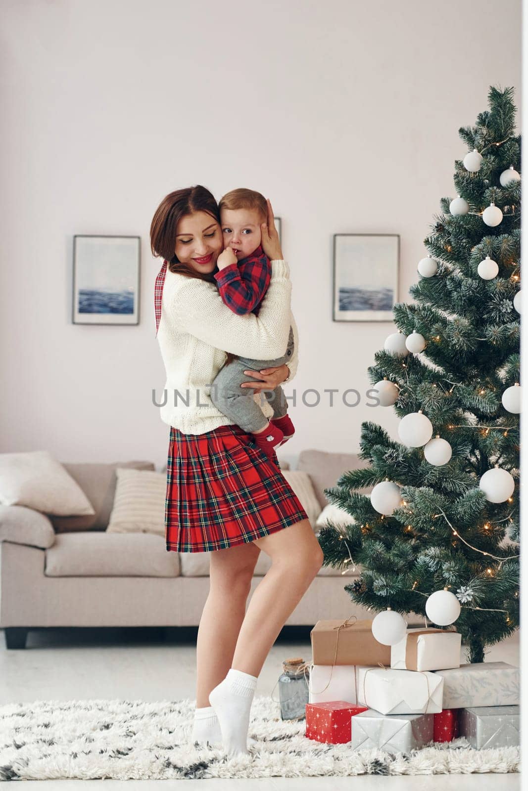 Beautiful young mother holds her little son by hands at home near New year christmas tree.