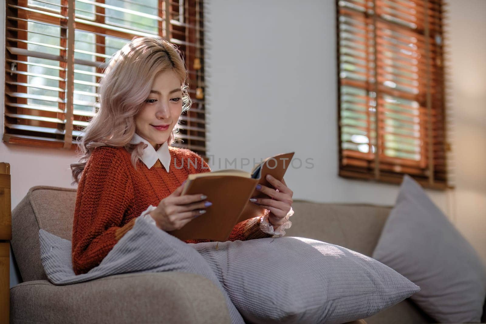 Attractive young Asian woman sits in the minimal and comfortable living room enjoying reading a book. by wichayada