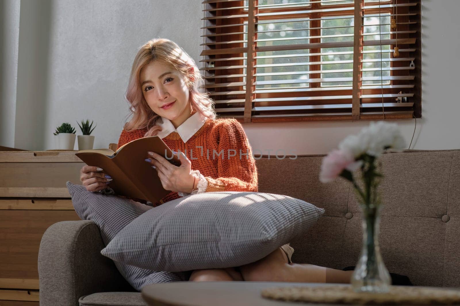 Attractive young Asian woman sits in the minimal and comfortable living room enjoying reading a book. by wichayada