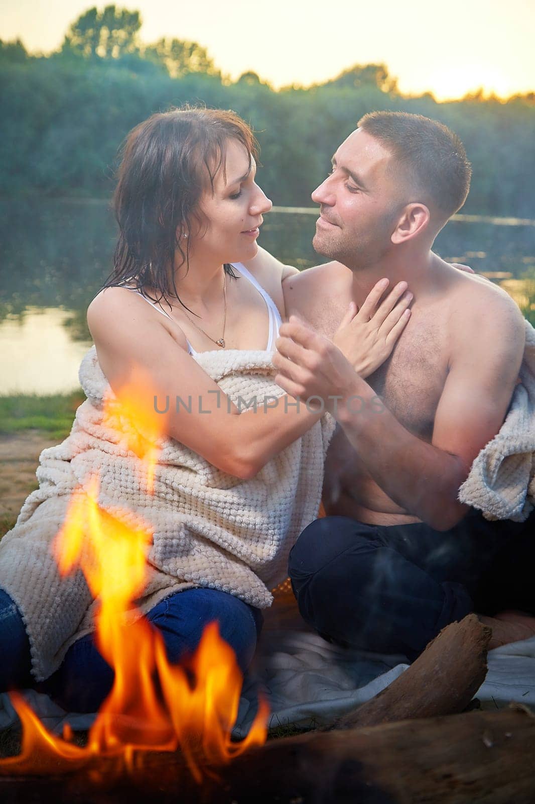 Happy Couple relaxin, having fun and hugs with fire in camping on nature near water of river or lake in summer sunny evening in sunset. Family or lovers have date and rest outdoor. Concept of love