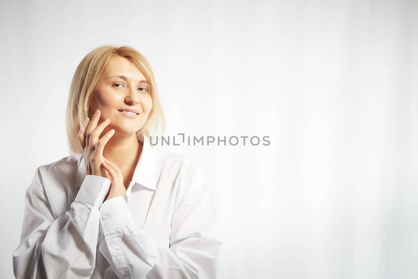 Portrait of a pretty calm sweet blonde smiling woman posing on a white background. Happy girl model in white shirt in studio. Copy space by keleny