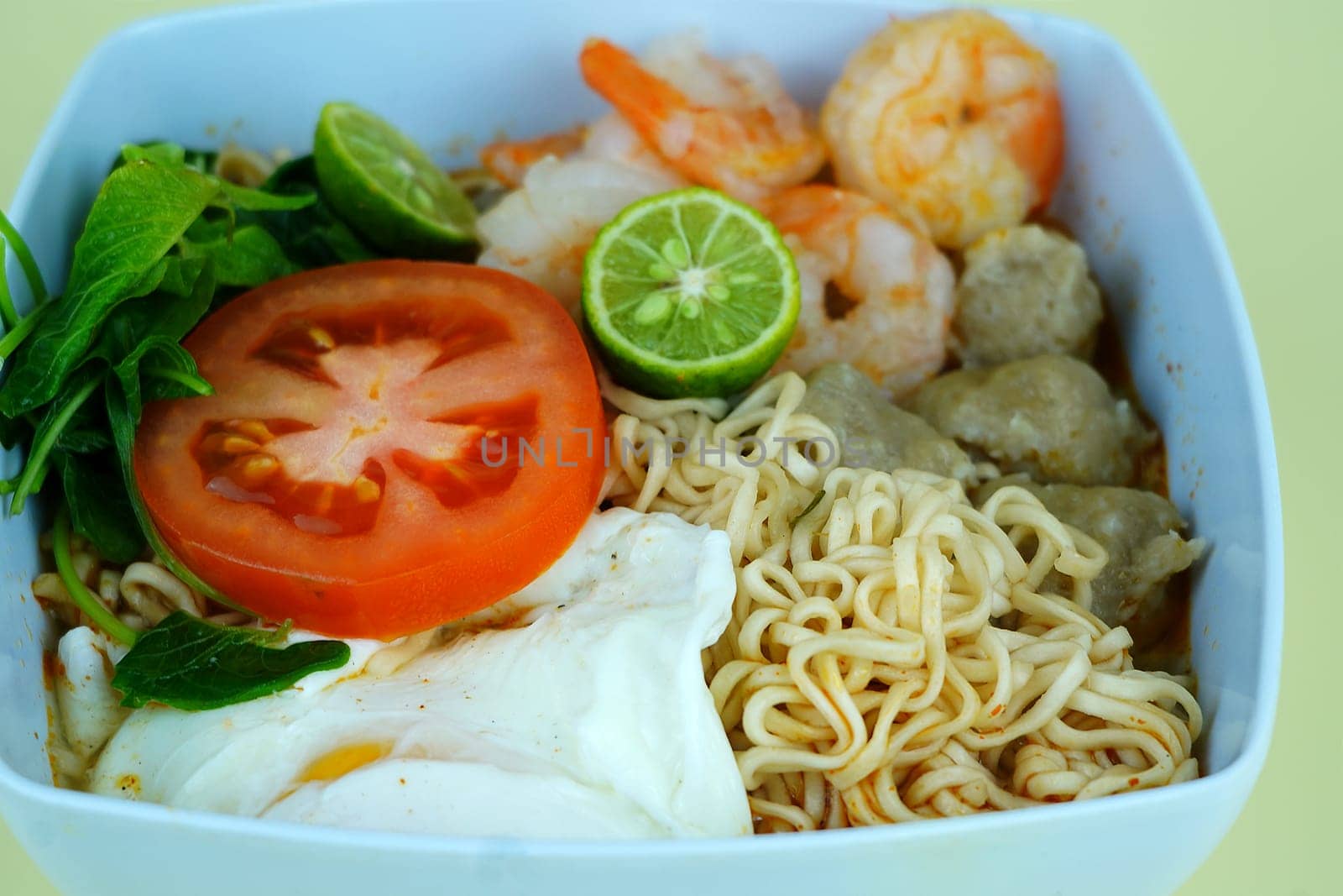 Soup noodle with shrimps, meat balls, eggs and vegetables served in white bowl.