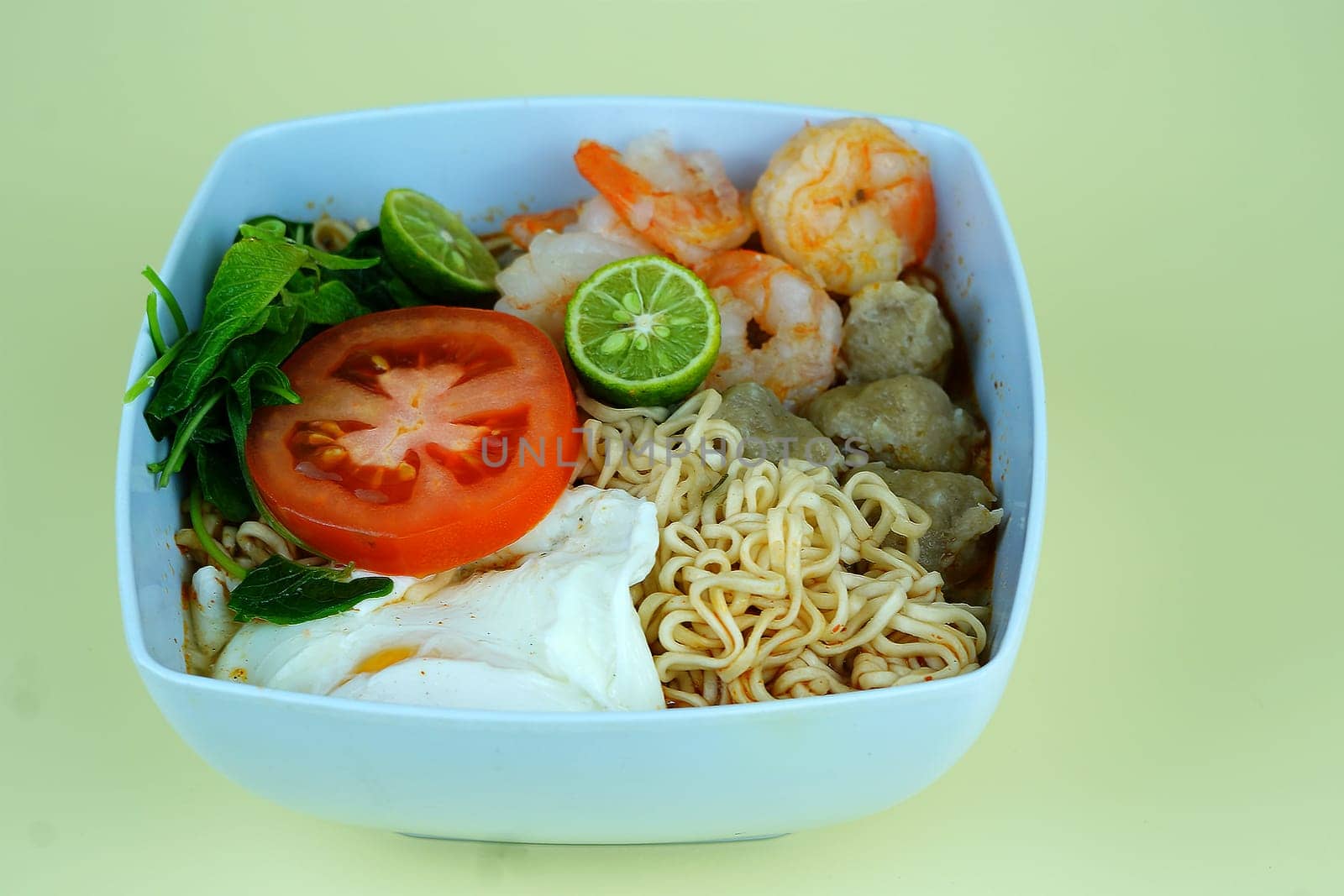 Soup noodle with shrimps, meat balls, eggs and vegetables served in white bowl.
