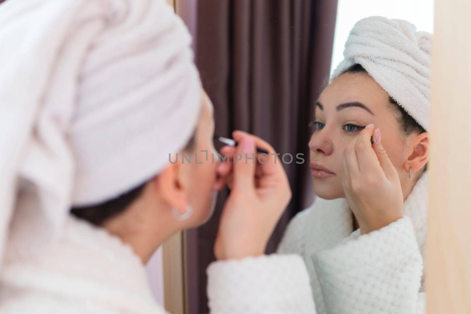 A woman applies black mascara to her eyelashes with a makeup brush. Young beautiful woman applying mascara makeup on her eyes in the bathroom.