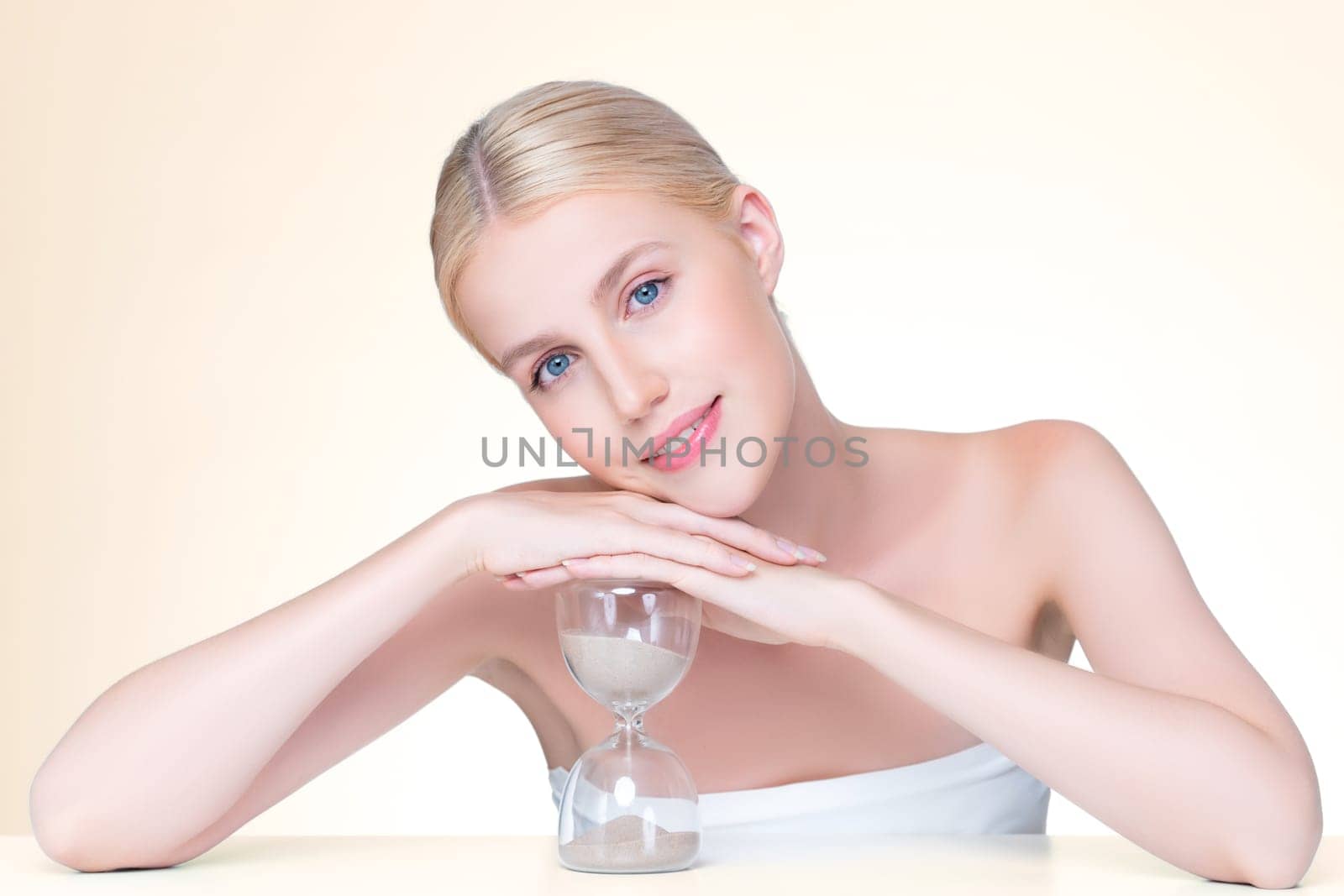 Personable model holding hourglass in beauty concept of anti-aging skincare treatment for woman. Young girl portrait with perfect smooth clean skin and flawless soft makeup in isolated background.