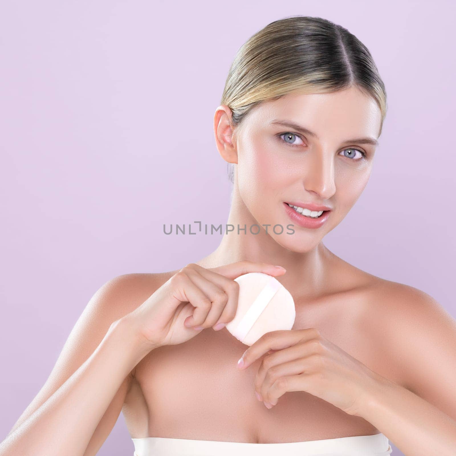 Alluring beautiful female model applying powder puff for facial makeup concept. Portrait of flawless perfect cosmetic skin woman put powder foundation on her face in pink isolated background.