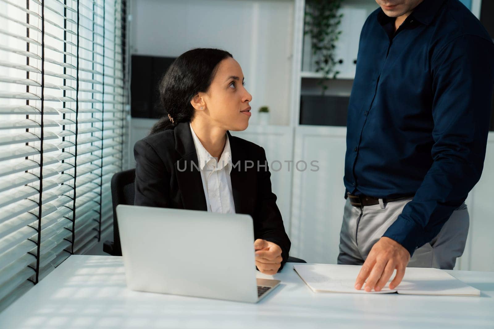 Competent female employee discussing with her colleague, employer using laptop at her office. Interpersonal relations among coworkers.