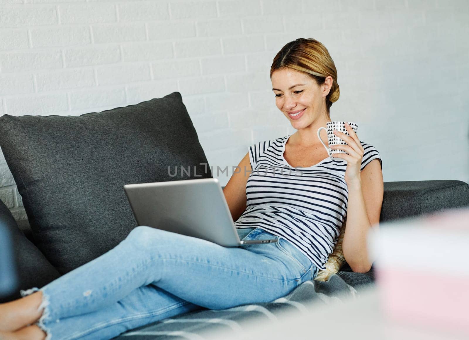 Woman Using Her Laptop On The Couch And Smiling