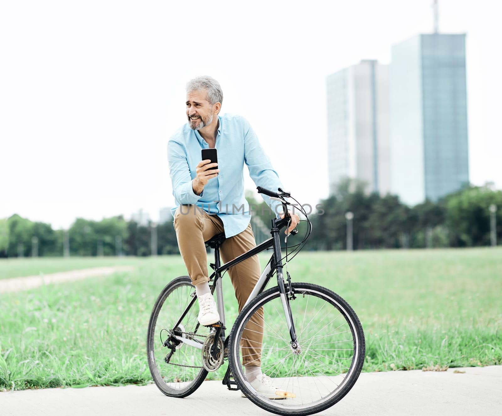 portrait of a senior man on bicycle using a cell phone in the city