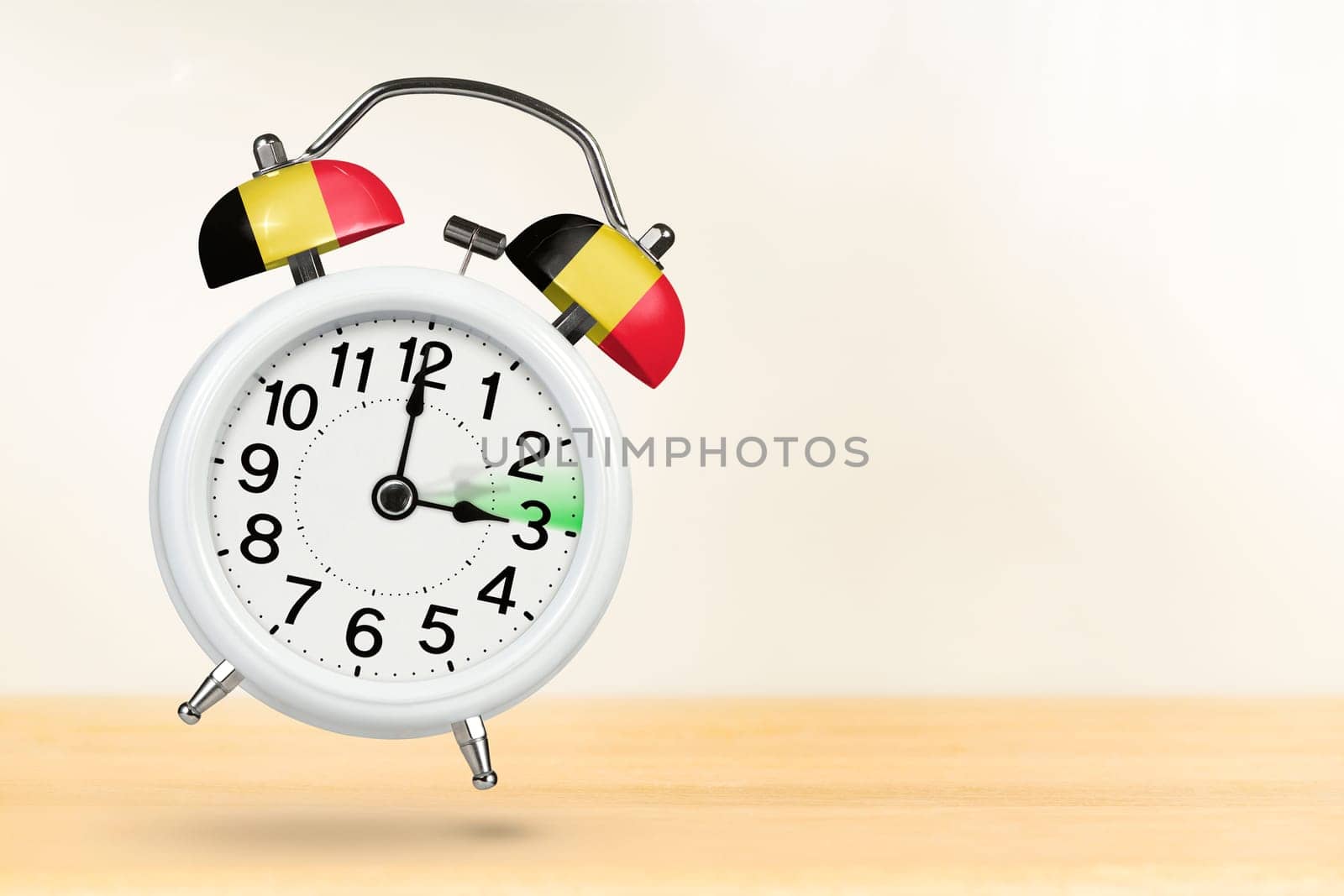 Time change in Belgium, spring forward. Summer time concept, over white background. A white alarm clock with a minute hand indicates that the time has been moved forward an hour with copy space. by SERSOL