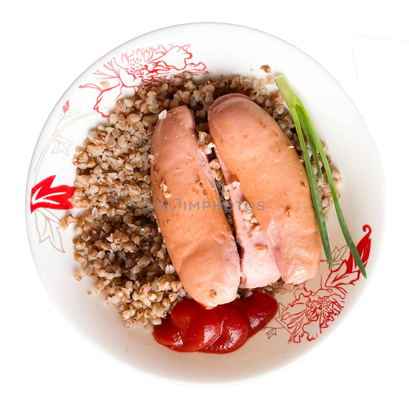 A plate of buckwheat and wieners with ketchup and a stalk of green onions on a white background.