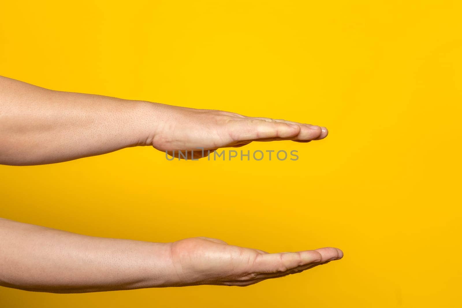 Strong hands of man in parallel offering something imaginary inside, advertising concept with copy space. Isolated on yellow background