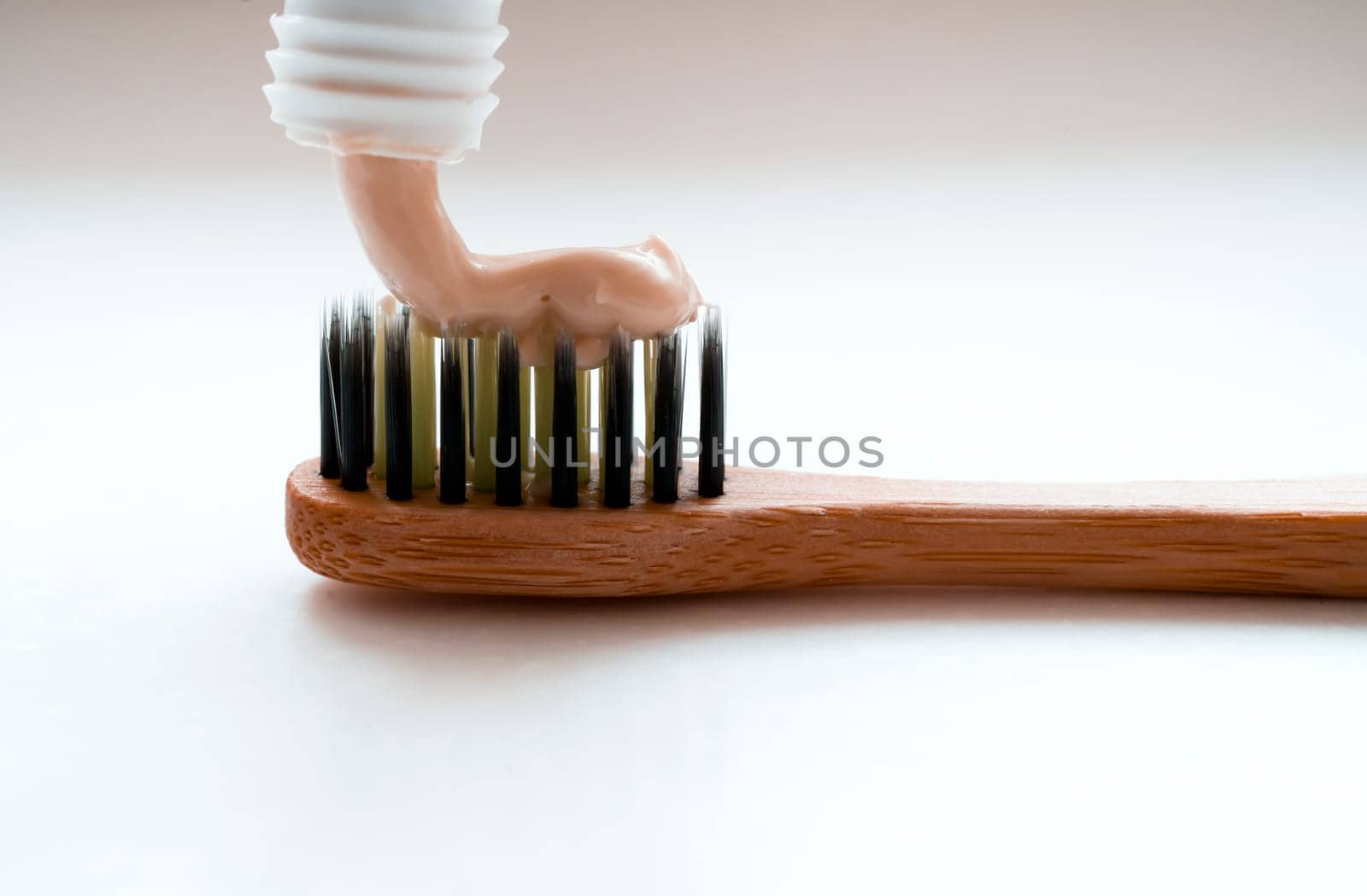 Stylish bamboo toothbrush on a light background in the bathroom with a toothpaste from a tube, close-up macro view.