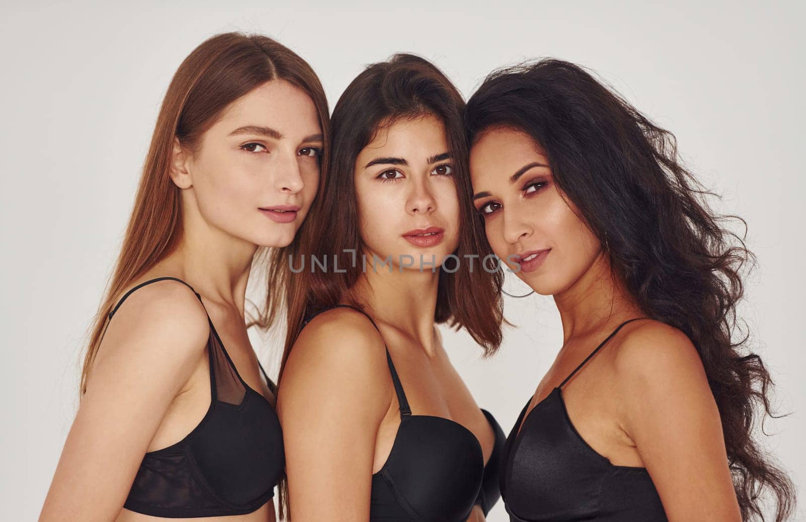 In black bra. Three young women in lingerie together indoors. White background.