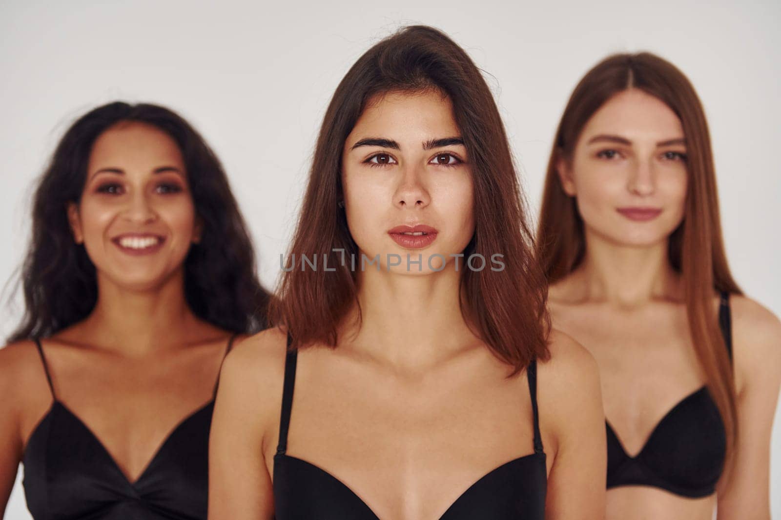 In black bra. Three young women in lingerie together indoors. White background by Standret