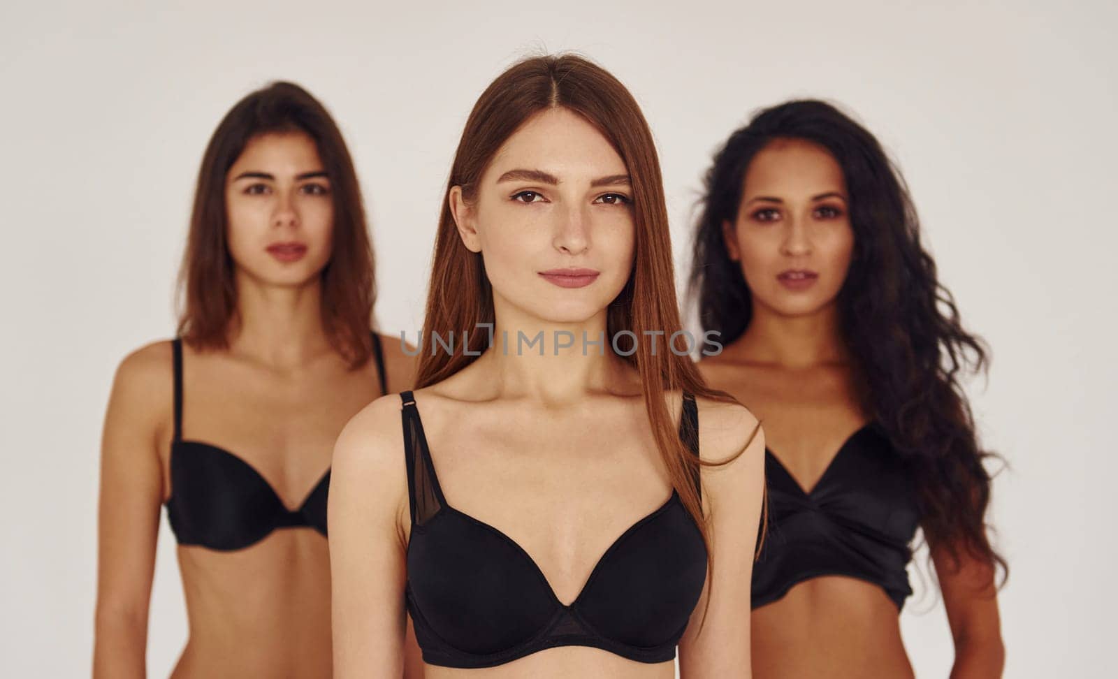 In black bra. Three young women in lingerie together indoors. White background by Standret