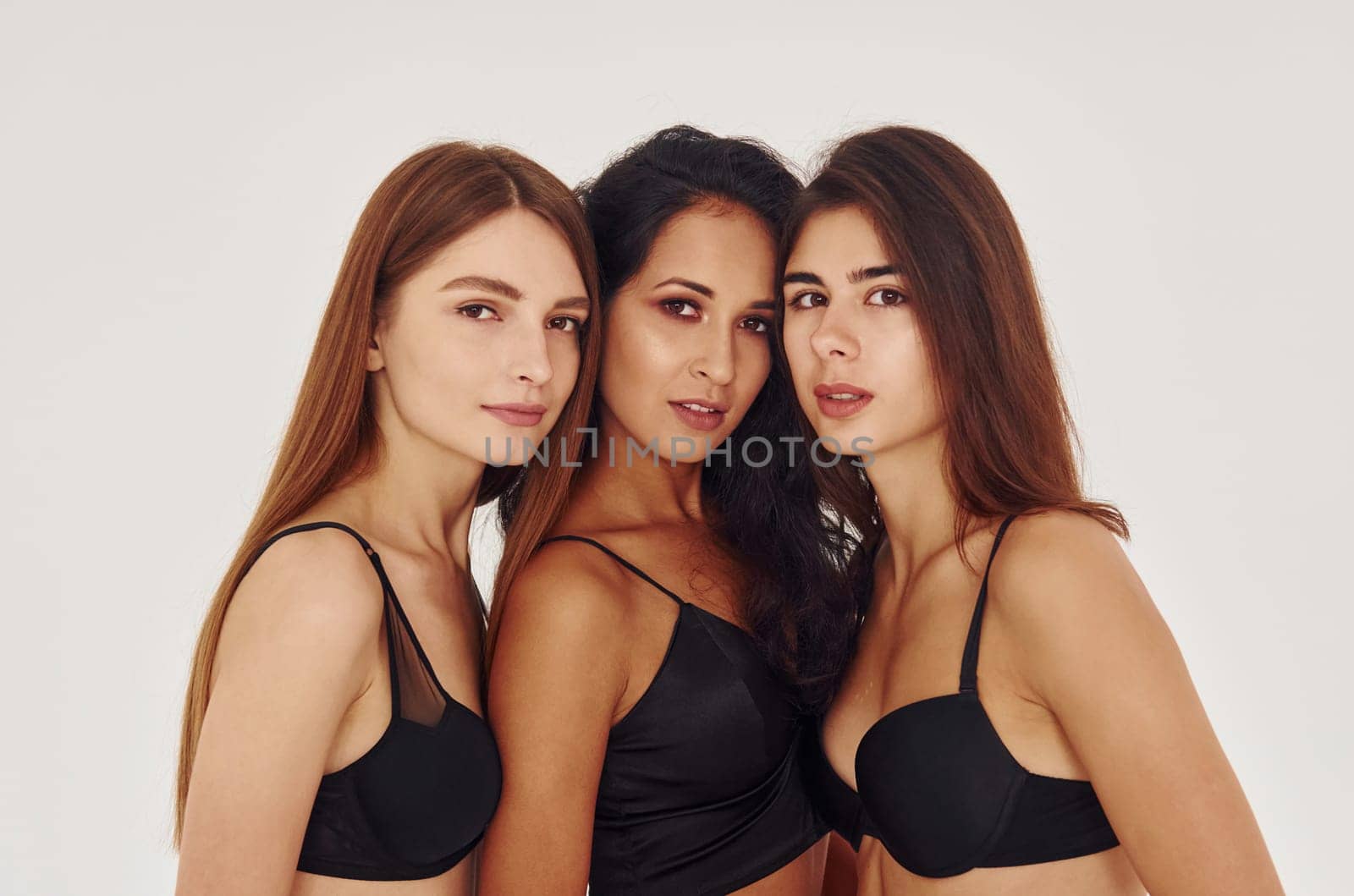 In black bra. Three young women in lingerie together indoors. White background by Standret