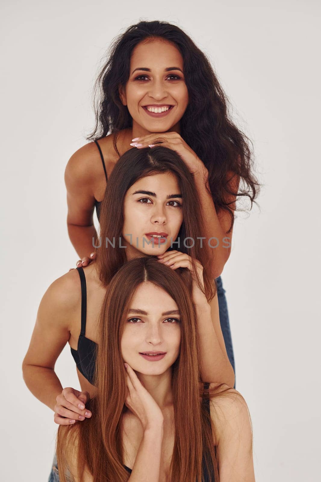 Three young women in lingerie together indoors. White background.