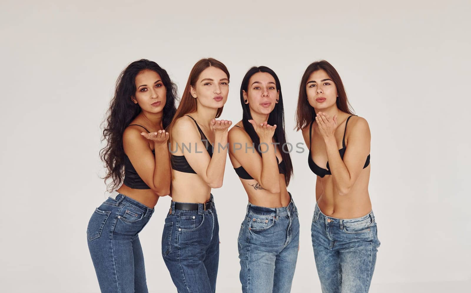 Air kiss. Four young women in lingerie together indoors. White background.