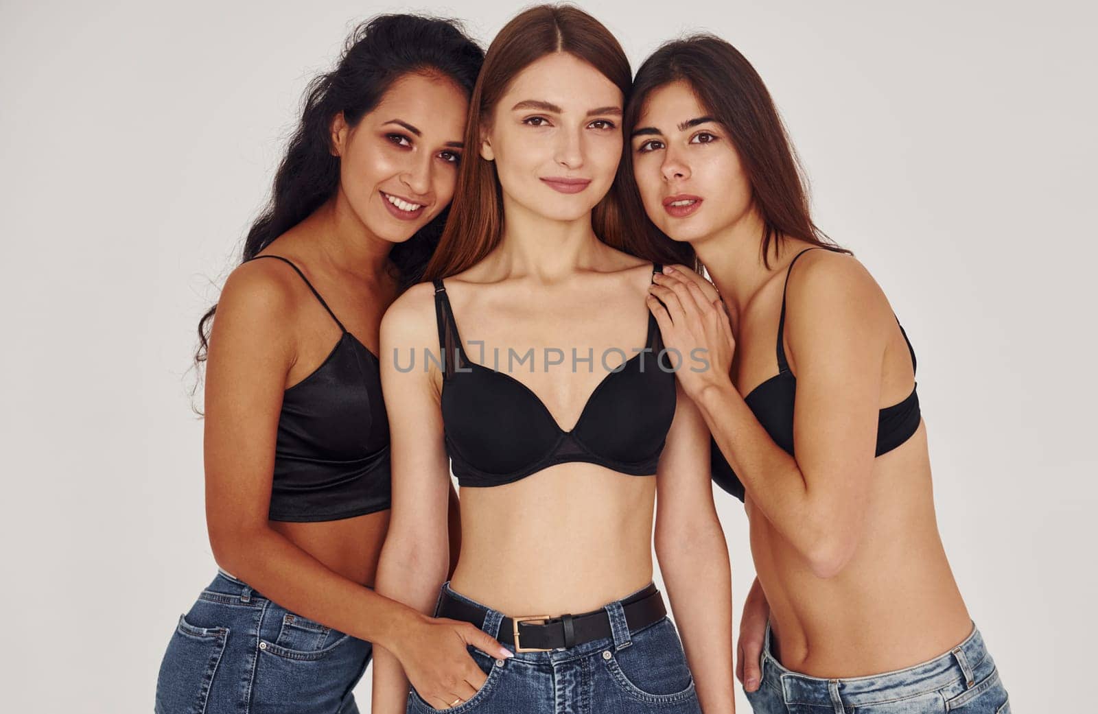 Embracing each other. Three young women in lingerie together indoors. White background by Standret