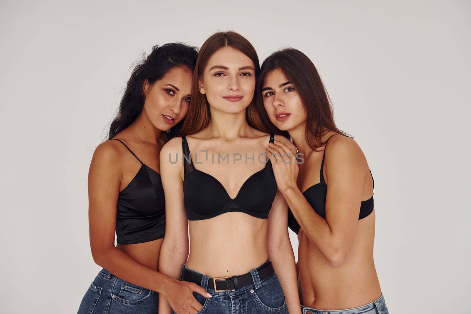 Embracing each other. Three young women in lingerie together indoors. White background by Standret