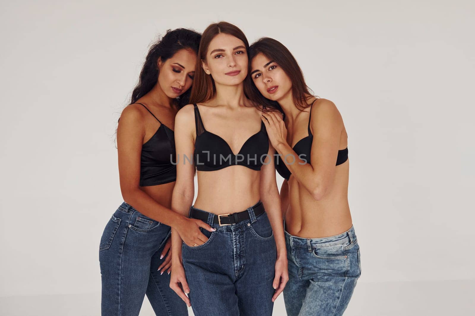 Embracing each other. Three young women in lingerie together indoors. White background.