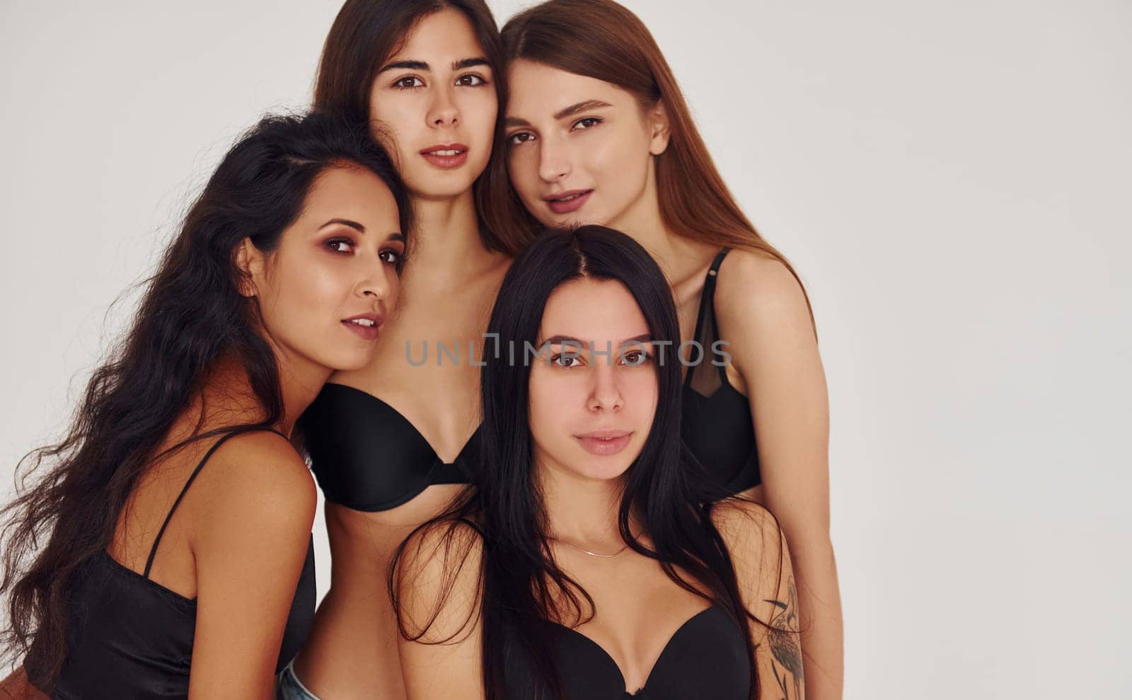 Leaning on each other. Four young women in lingerie together indoors. White background by Standret