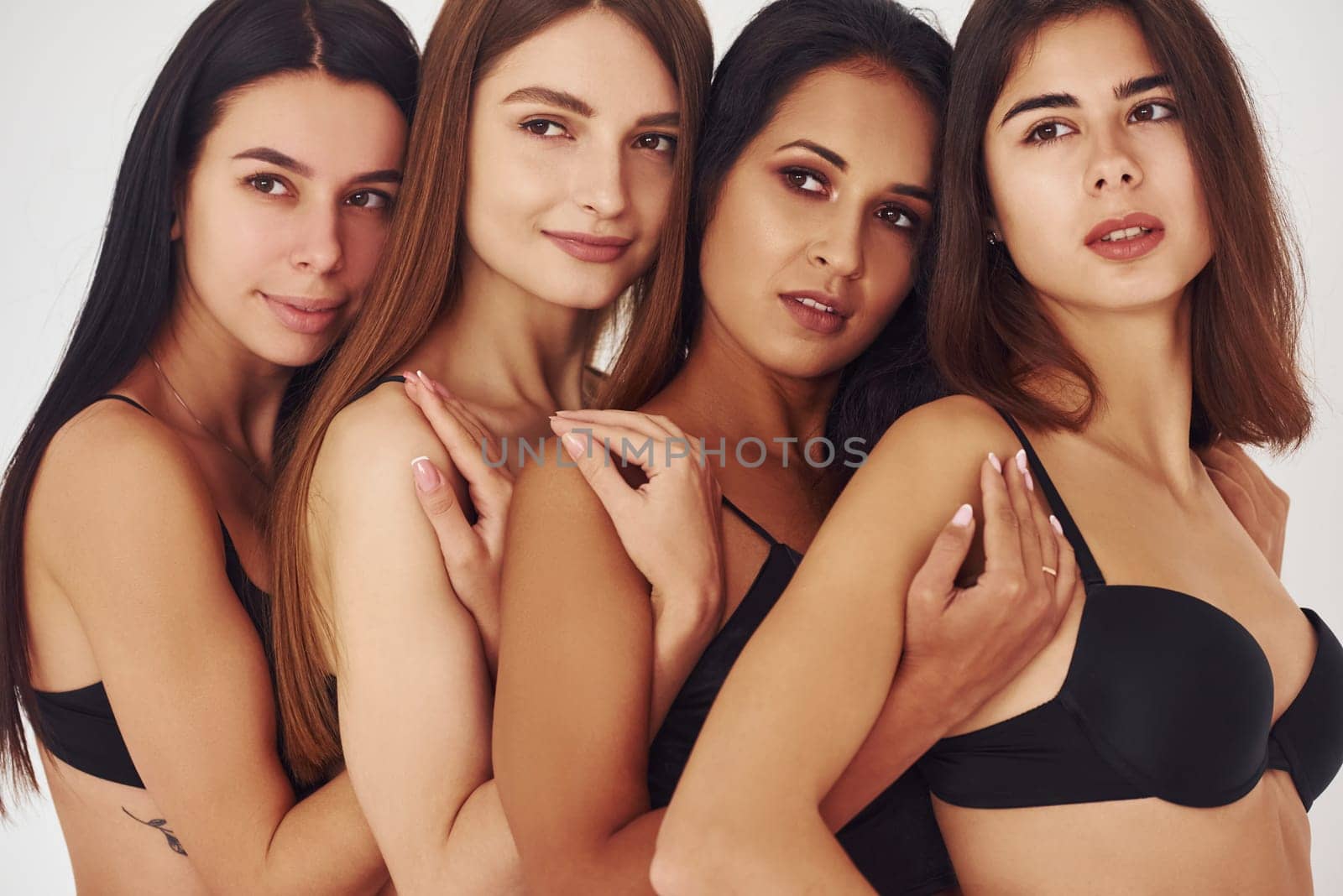 Leaning on each other. Four young women in lingerie together indoors. White background.