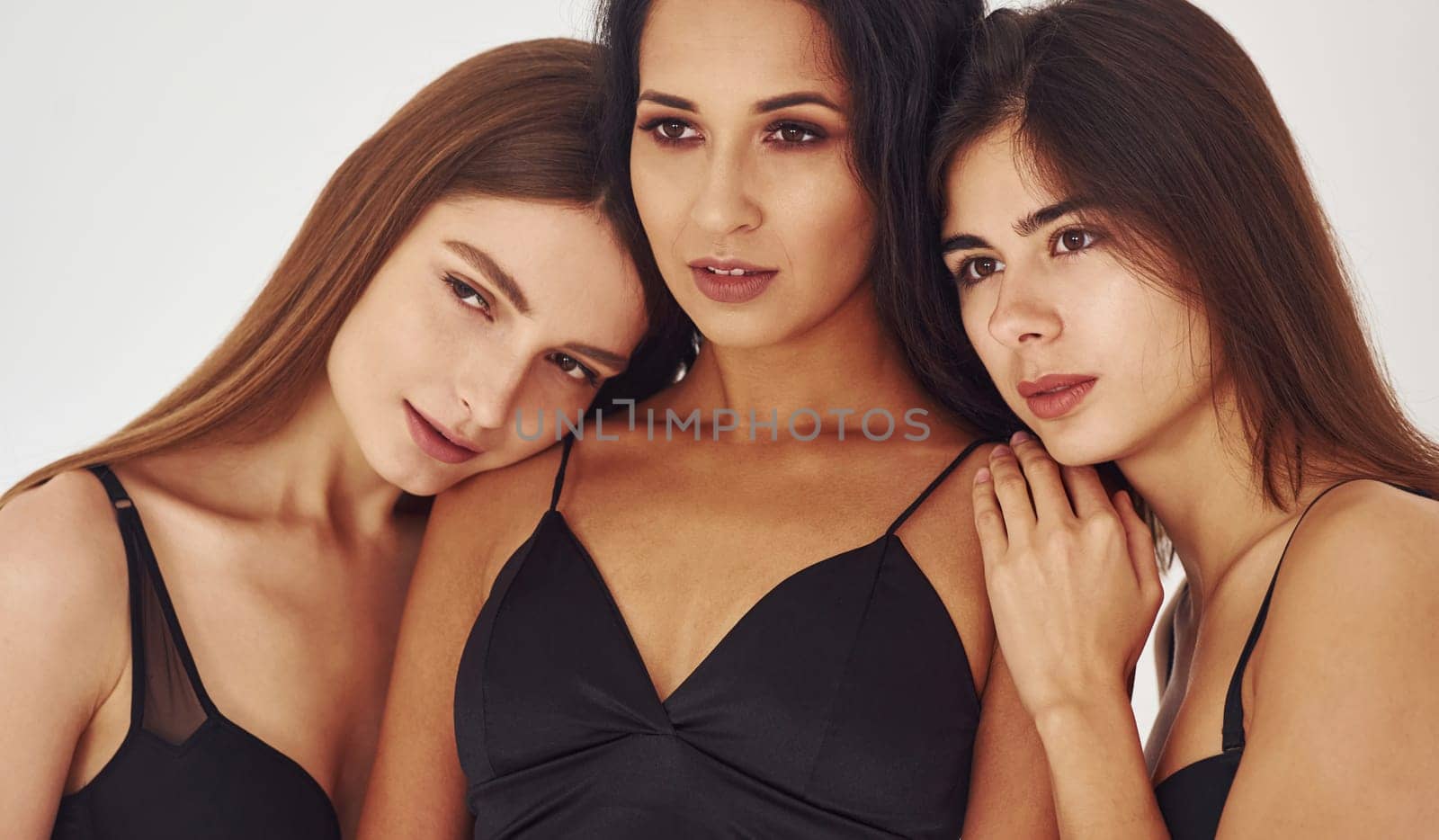 Three young women in lingerie together indoors. White background.