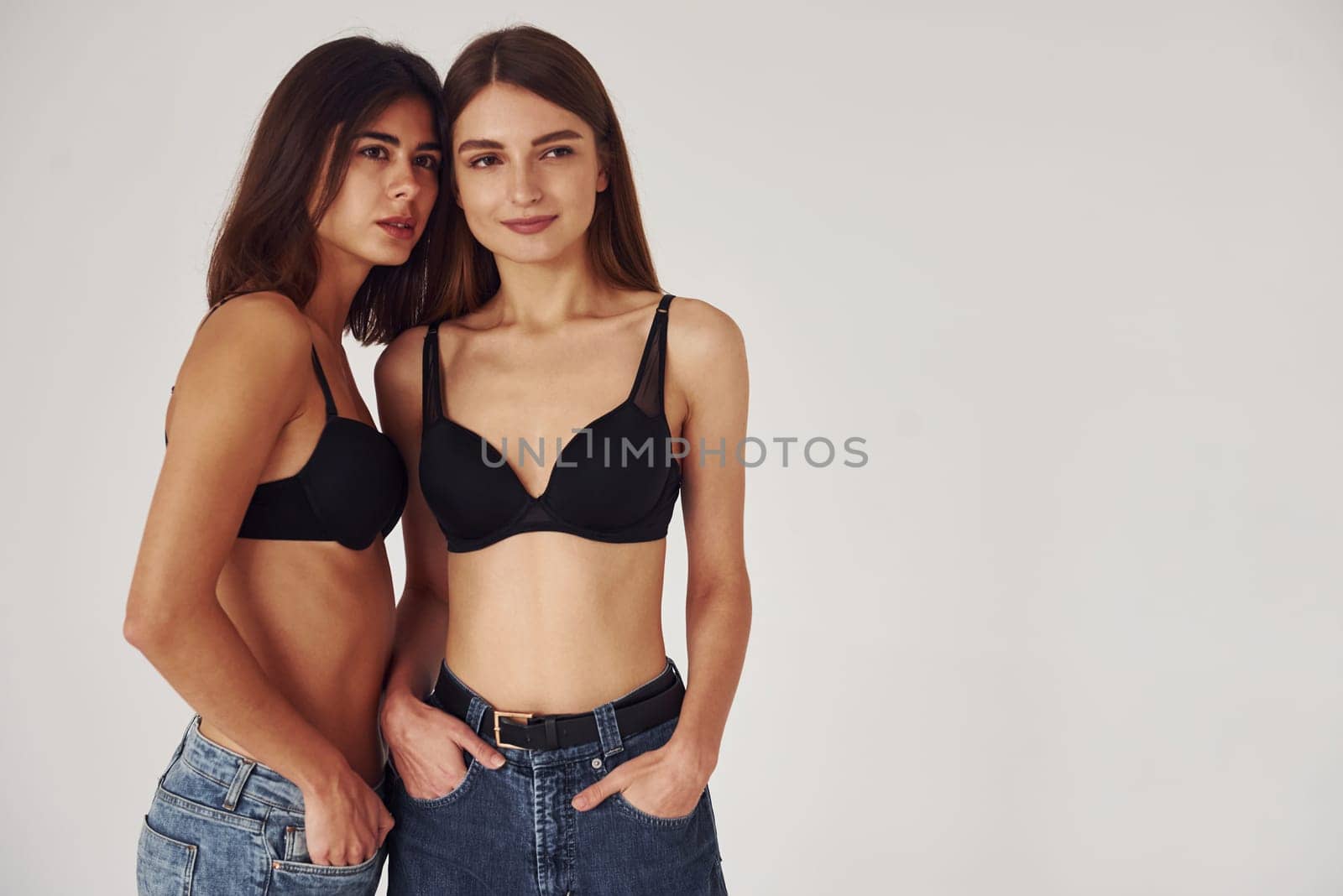 Two young women in lingerie together indoors. White background.