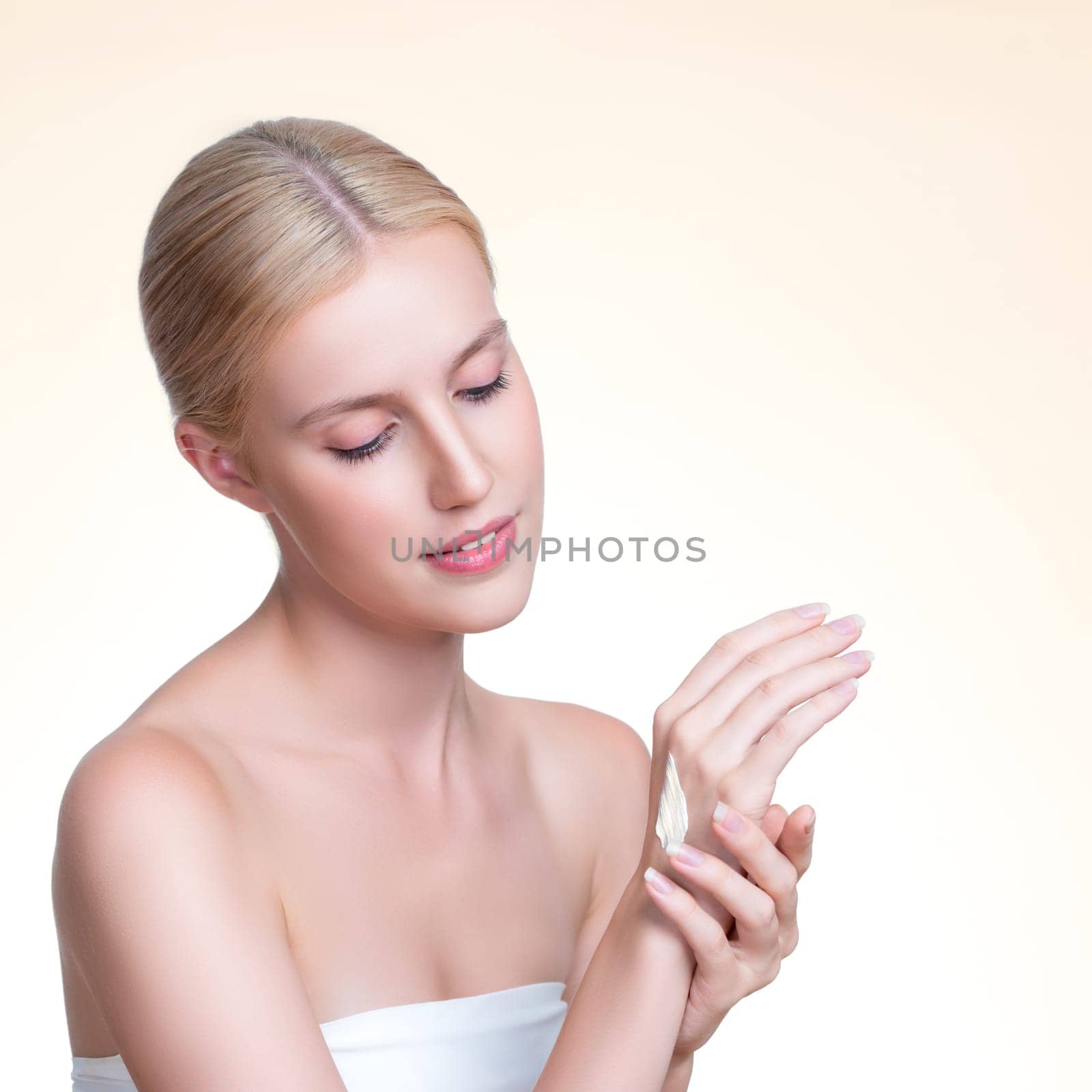 Personable woman applying moisturizer cream on her hand for perfect skincare treatment concept in isolated background. Beauty care cream applying on body by female model with soft natural makeup.