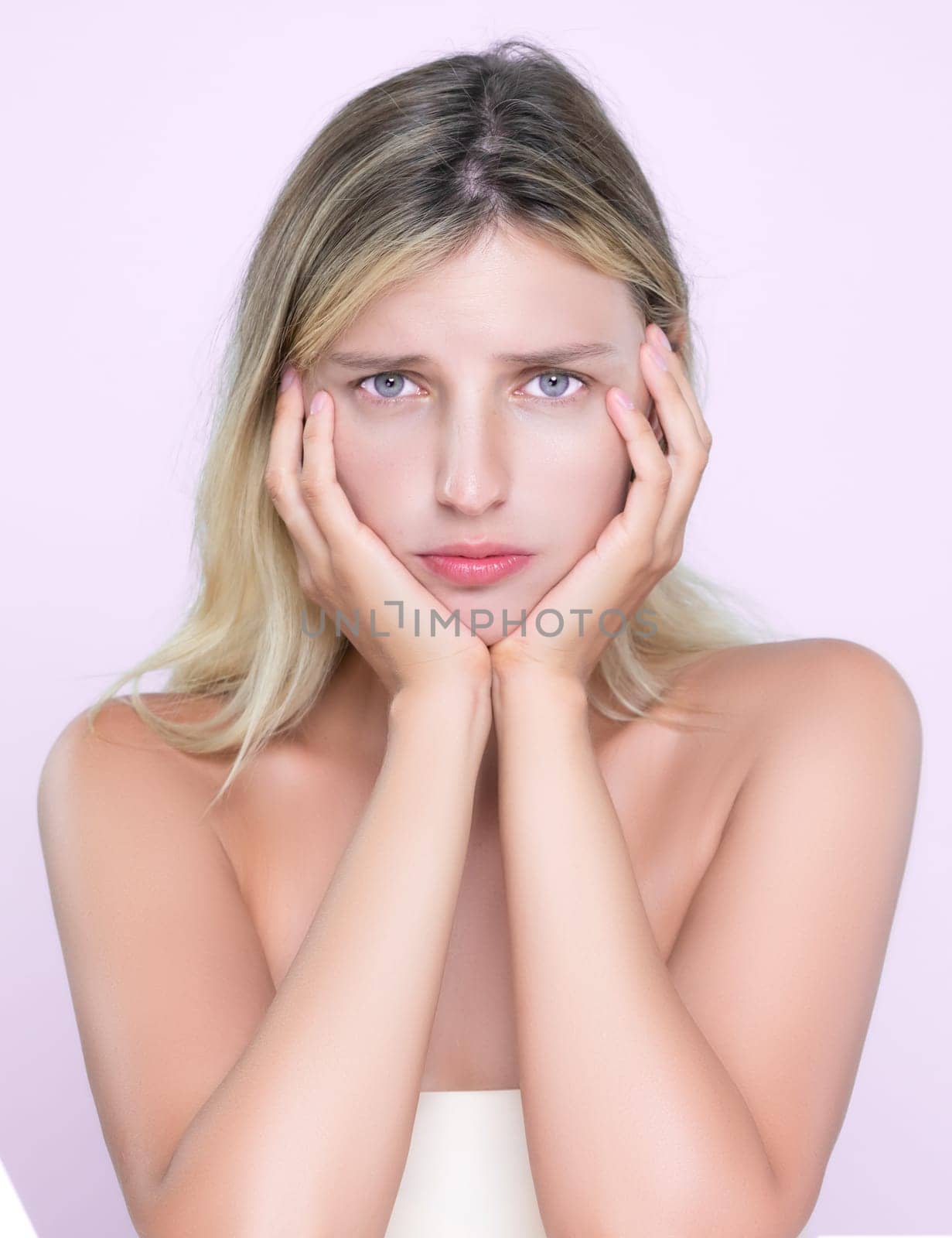 Alluring portrait of beautiful woman feel insecure on her facial skin, oily or acne problem. Worried female model with perfect smooth clean skin check her face on mirror in pink isolated background.