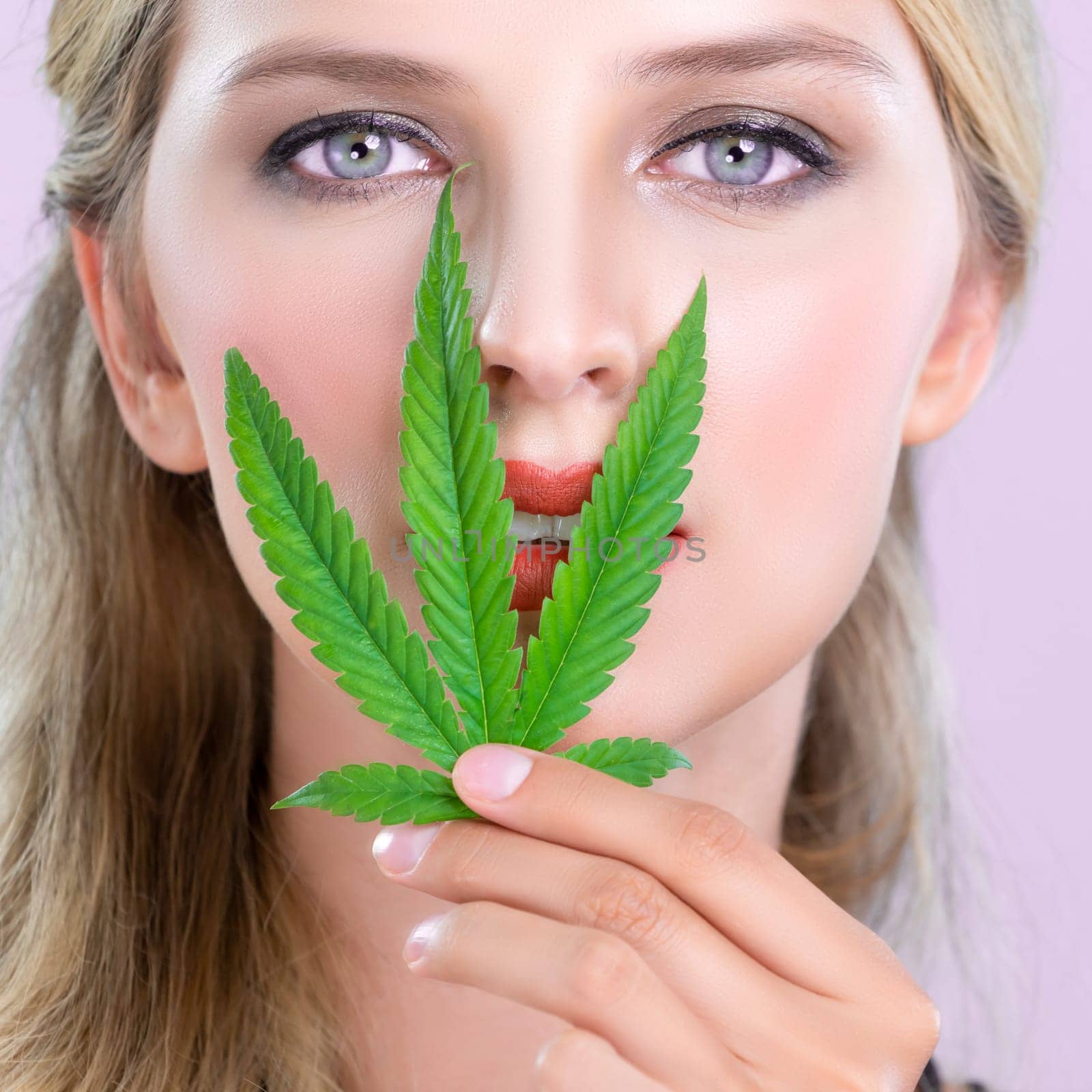 Closeup alluring beautiful woman portrait with perfect makeup lip stick, eyeshadow hold green leaf as concept for cannabis skincare cosmetic product for skin freshness treatment in isolated background