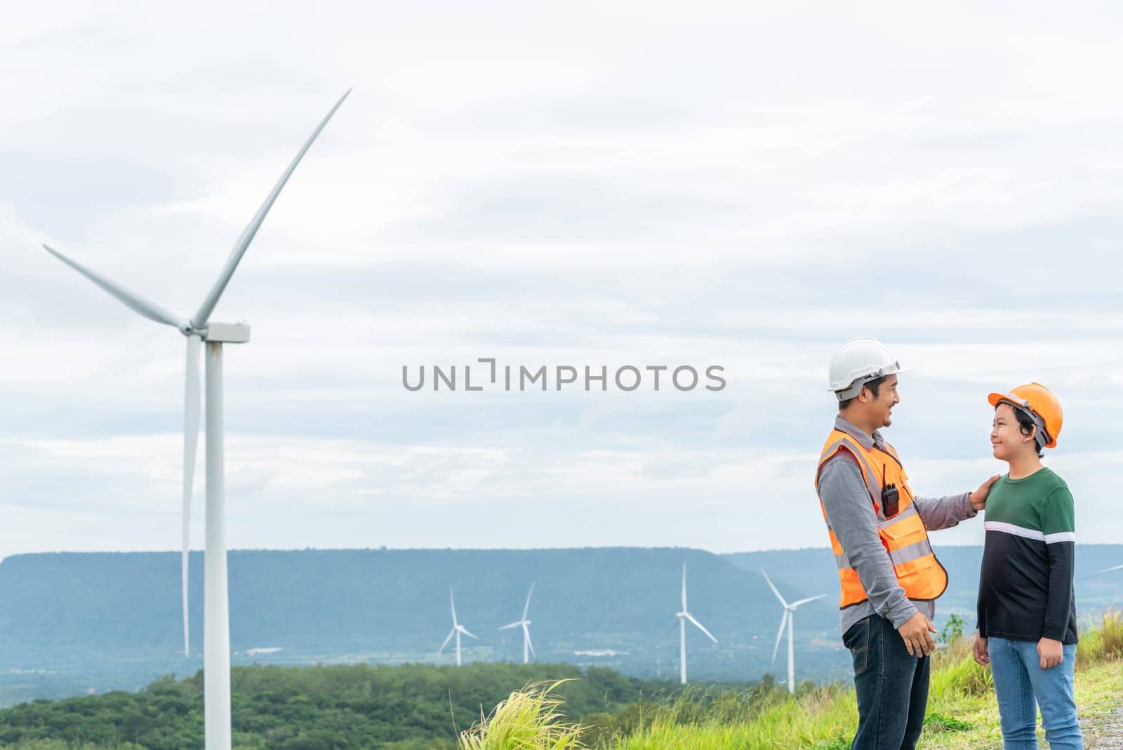 Engineer with his son on a wind farm atop a hill or mountain in the rural. Progressive ideal for the future production of renewable, sustainable energy. Energy generation from wind turbine.