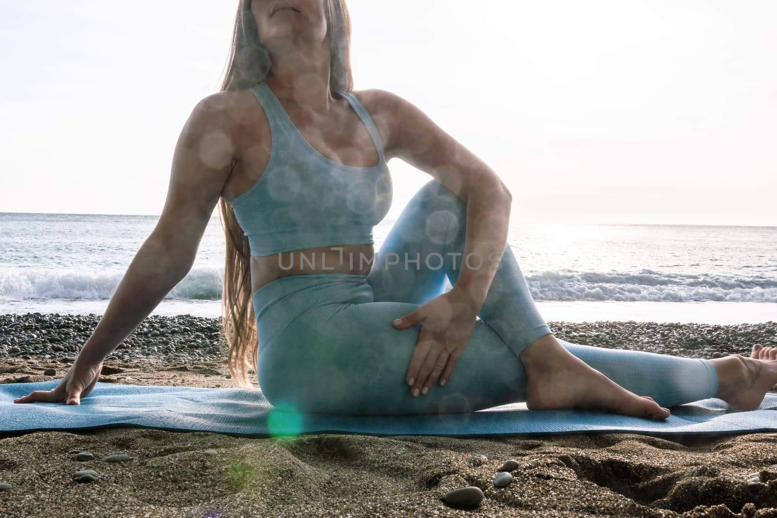 Middle aged well looking woman with black hair doing Pilates with the ring on the yoga mat near the sea on the pebble beach. Female fitness yoga concept. Healthy lifestyle, harmony and meditation.