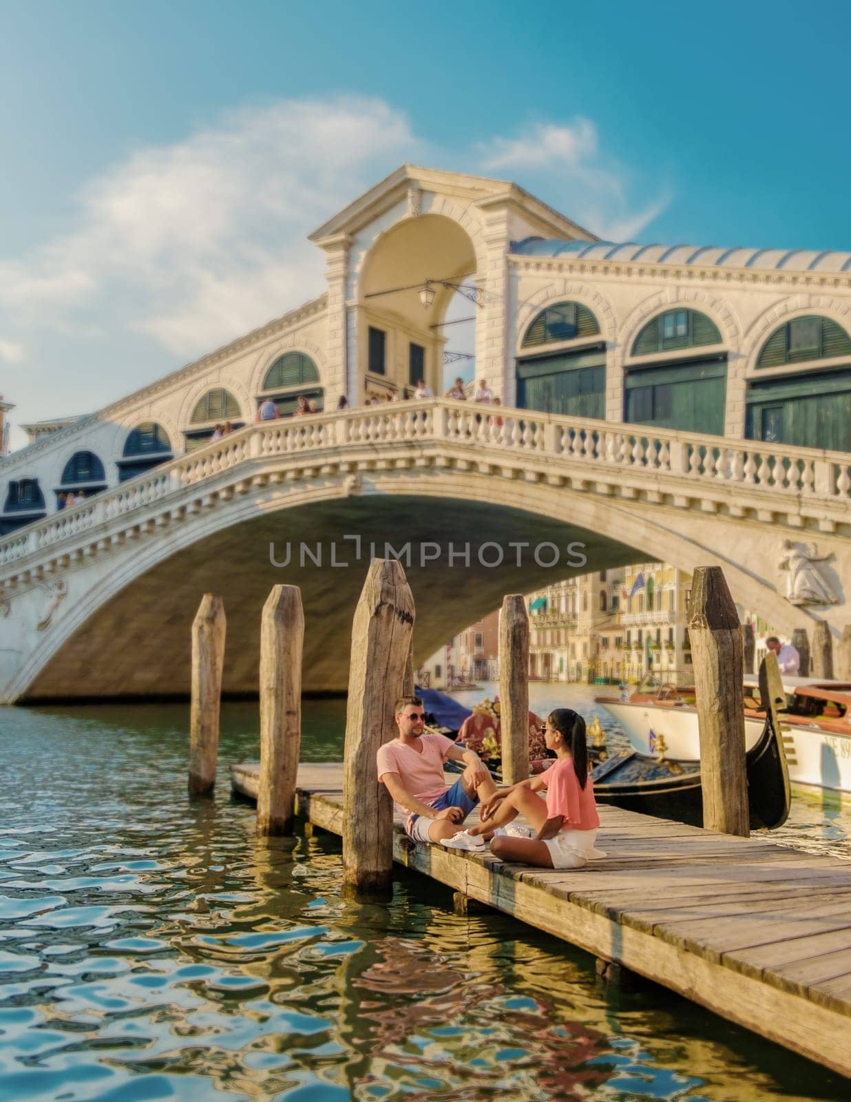 a couple of men and women on a city trip in Venice Italy sitting at the waterfront of the Rialto bridge in Venice, Italy. Architecture and landmark of Venice.cityscape of Venice Italy during summer