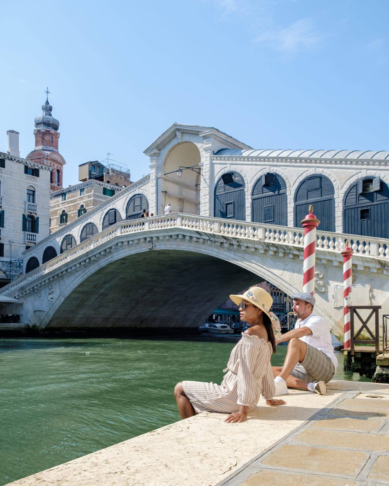 couple of men and women on a city trip in Venice Ital sitting at waterfront of the Rialto bridge by fokkebok