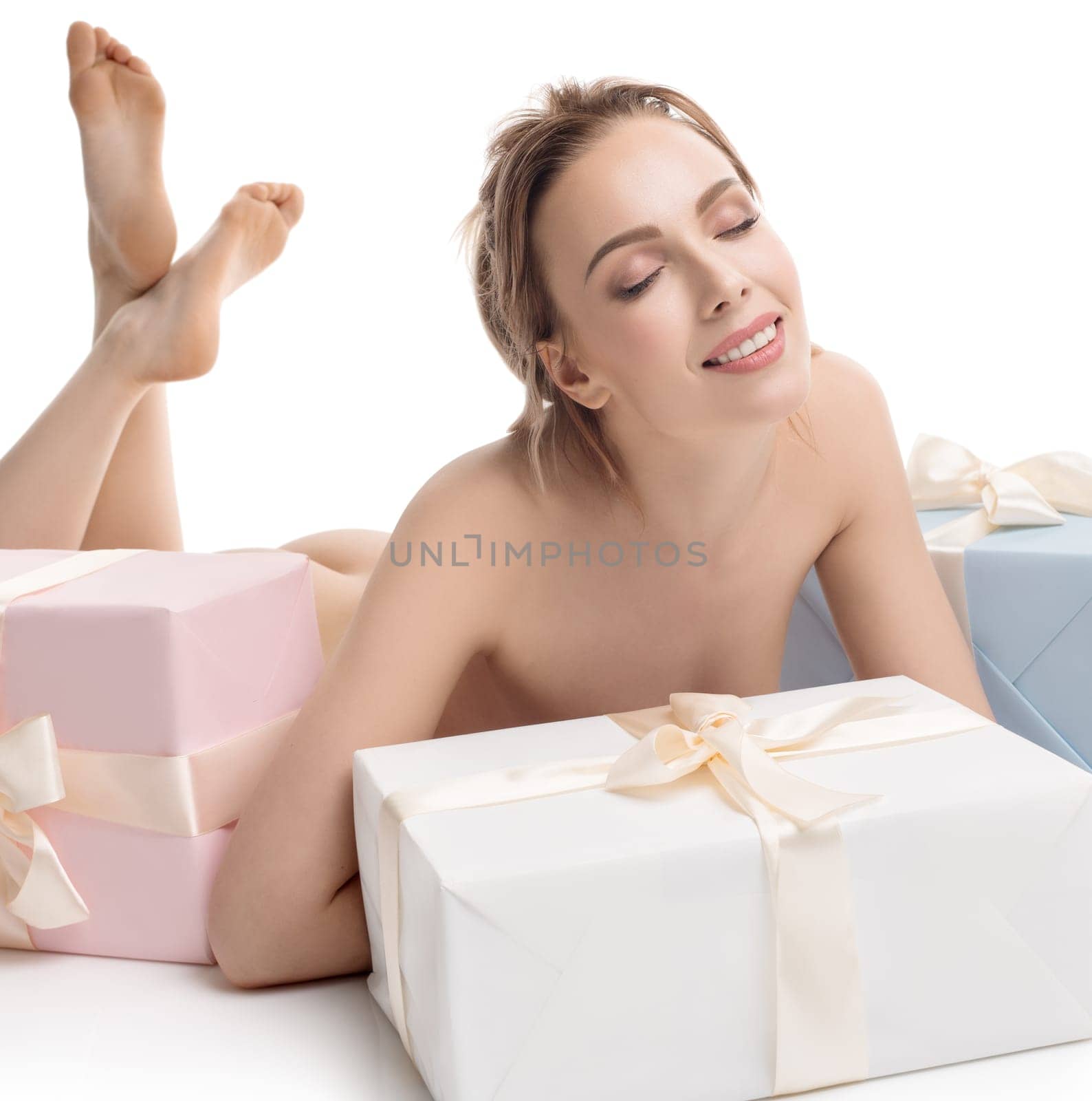 Nude pretty girl and several gift boxes tied up with beige ribbions lying on the floor isolated full-length shot on white background