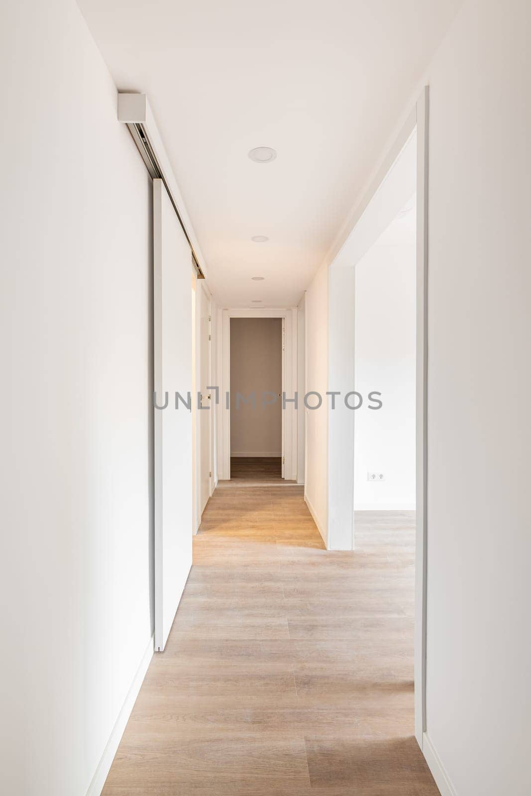 White corridor with entrances to bright room and slide doors in an empty apartment before moving or after renovation. Concept of renovation and restoration of old premises. Copyspace.