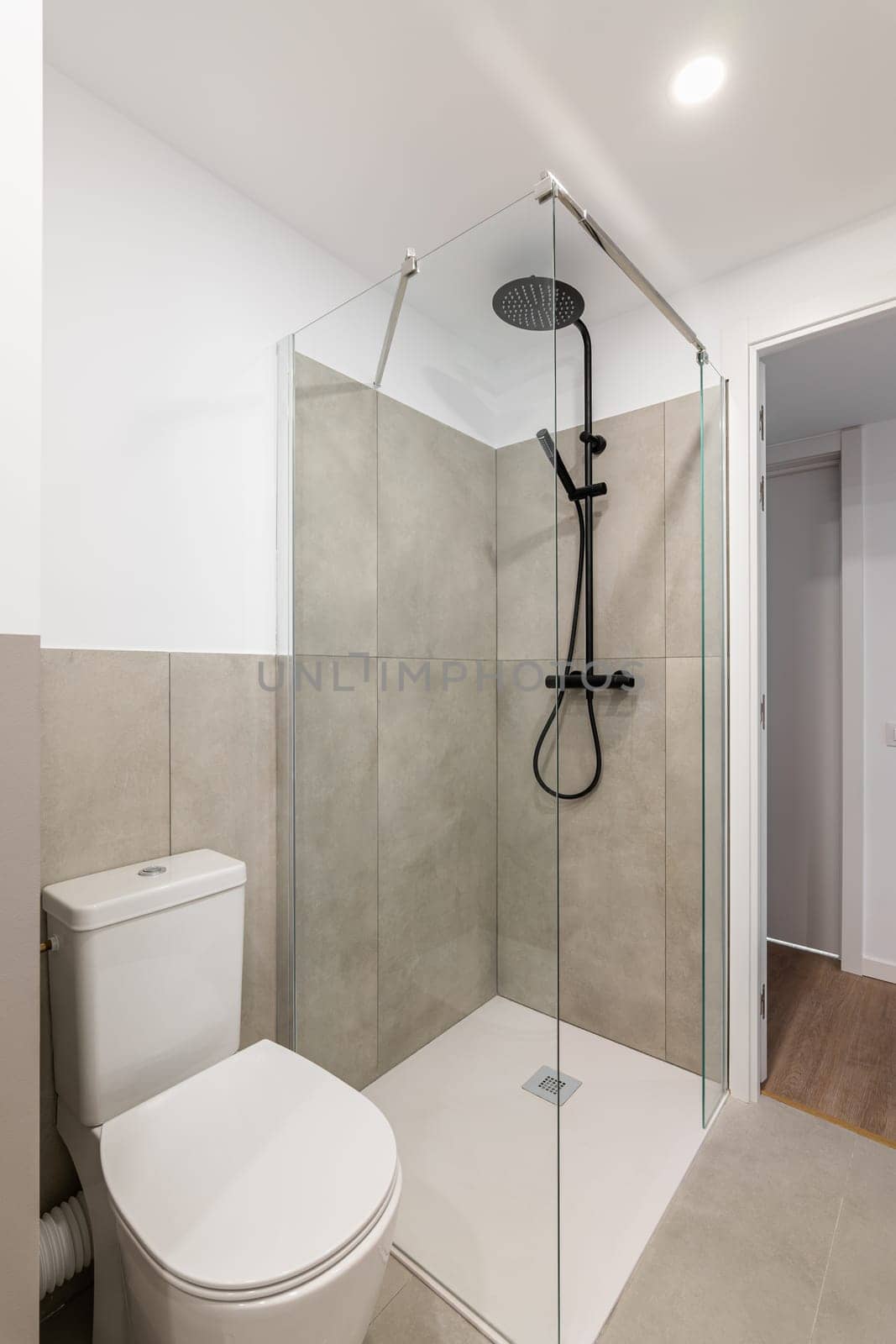 An empty tiny bathroom with a toilet and a glazed shower with gray tiles. The concept of a simple and stylish bathroom in an apartment or luxury hotel.