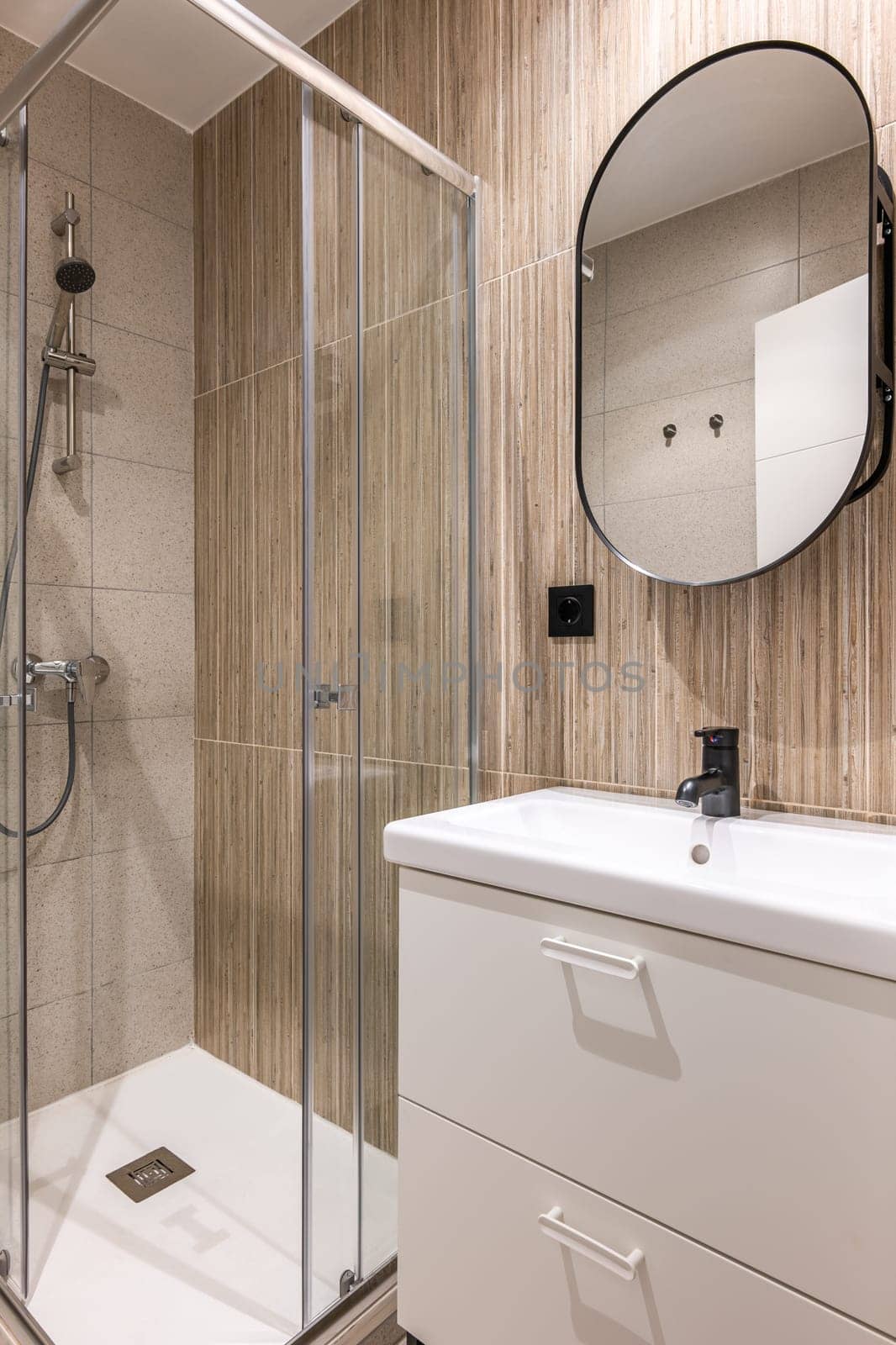 Close-up of small bathroom with trendy white glass shower cabinet and a ceramic sink with black tap and stylish beige tiles. Concept bathroom in a hotel or apartment.