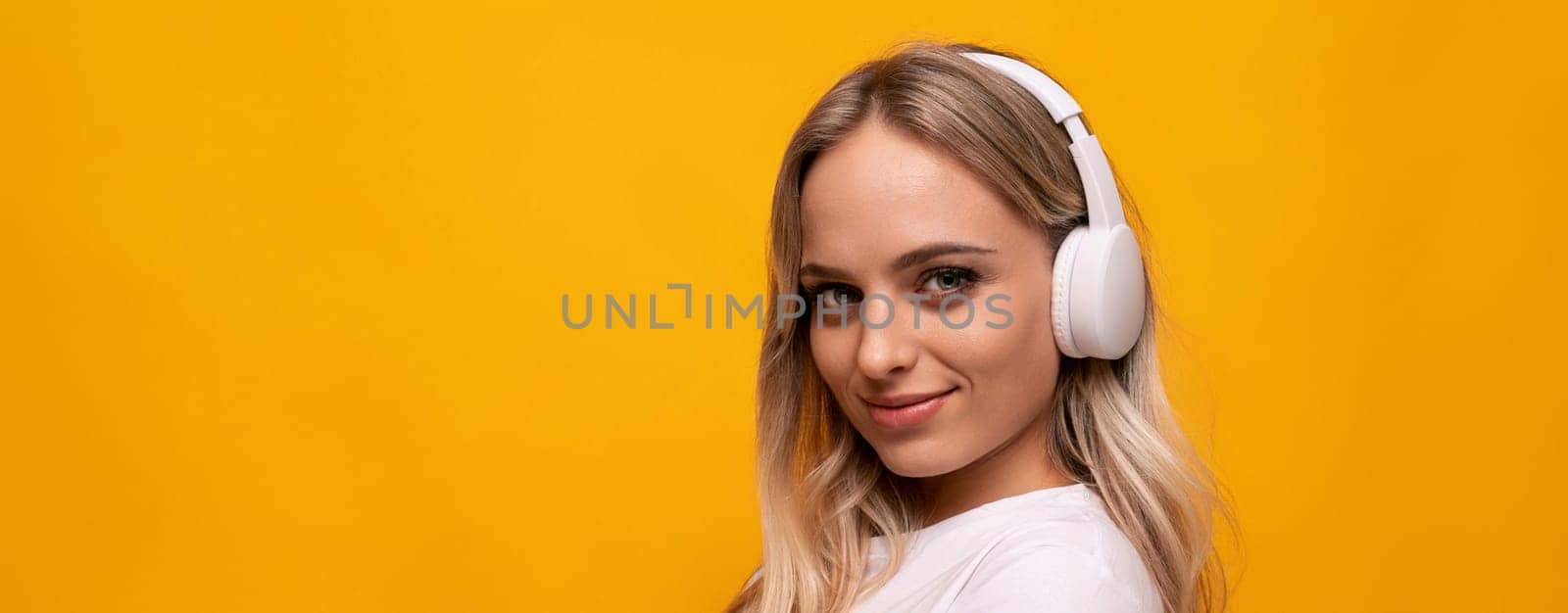 smiling woman listening to music in white headphones on orange background with empty space by TRMK